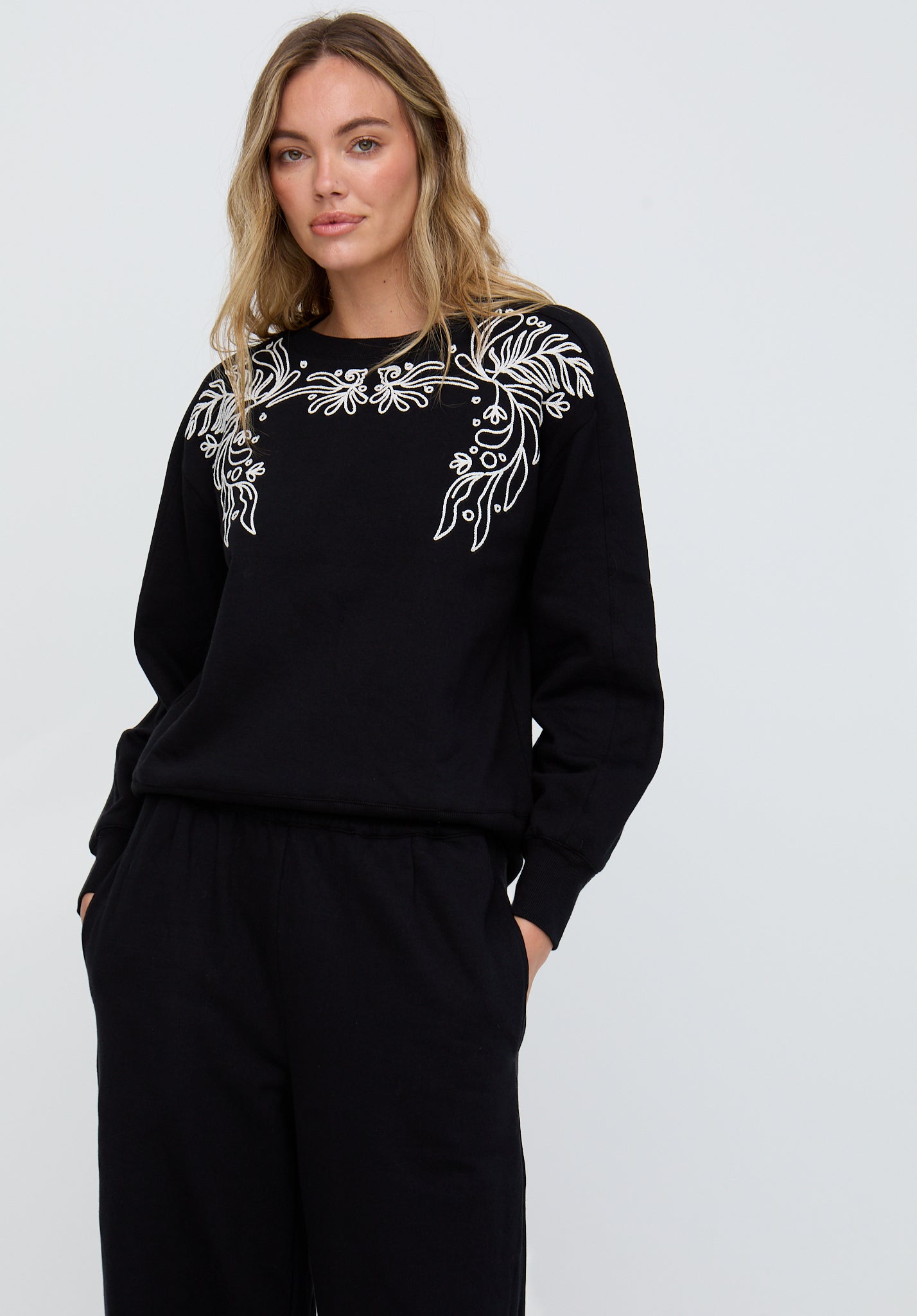 Woman wearing a black outfit with white floral embroidery on a plain background