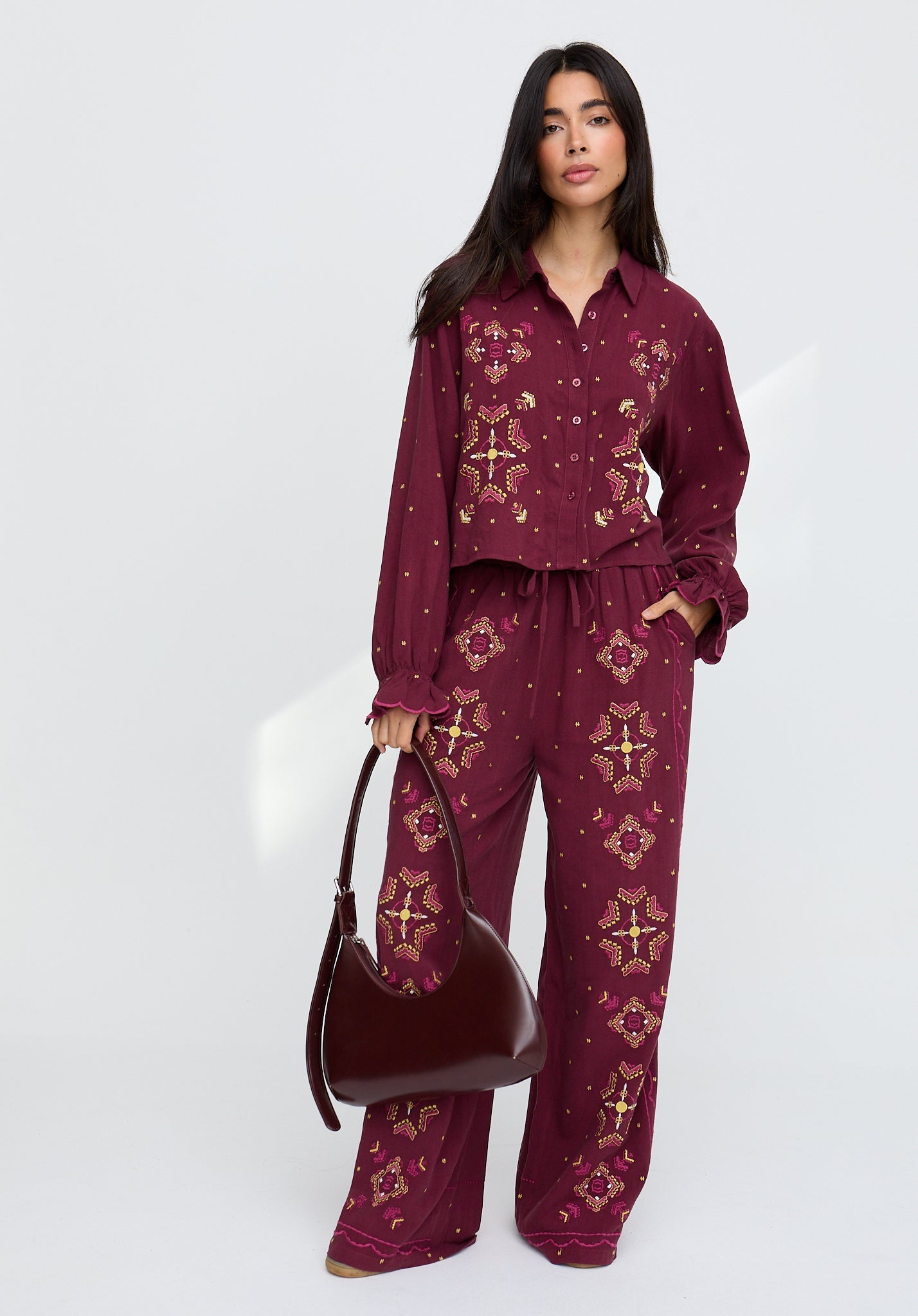 Woman wearing a burgundy patterned outfit with a matching handbag on a white background
