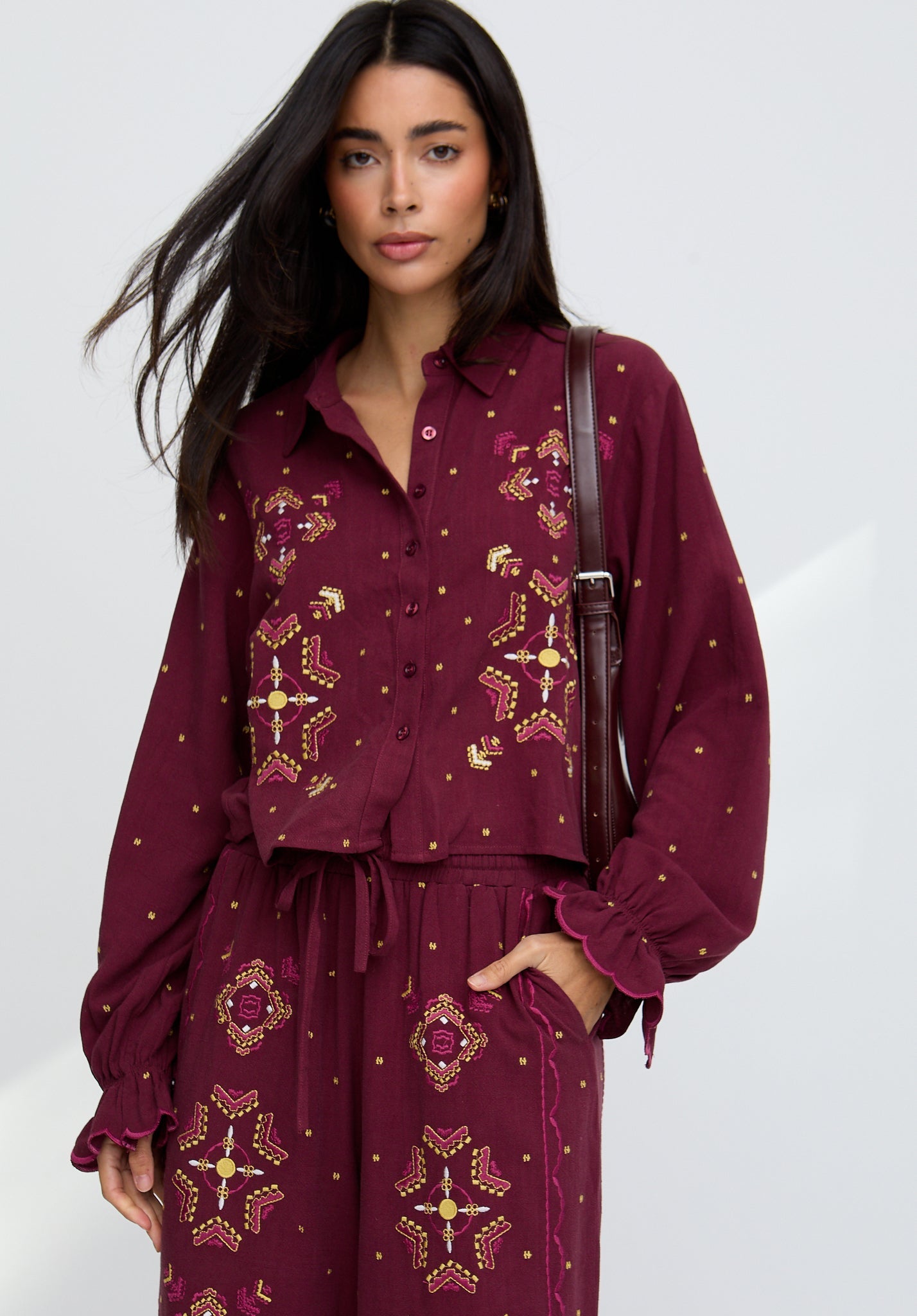 Woman wearing a burgundy outfit with gold embroidery on a white background