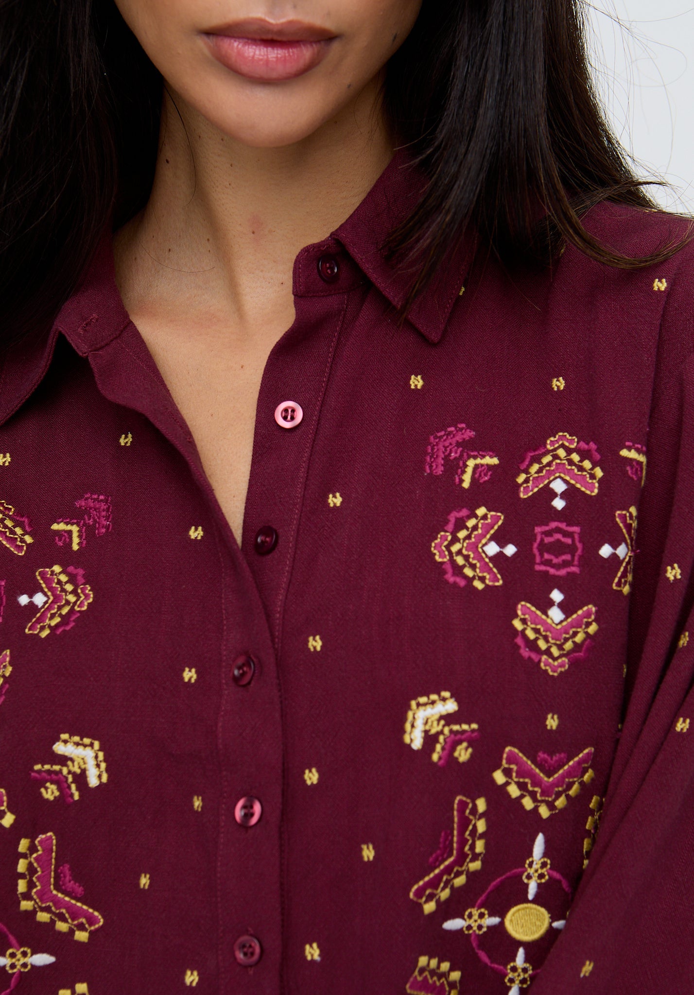 Close-up of a person wearing a maroon shirt with intricate gold and pink patterns.