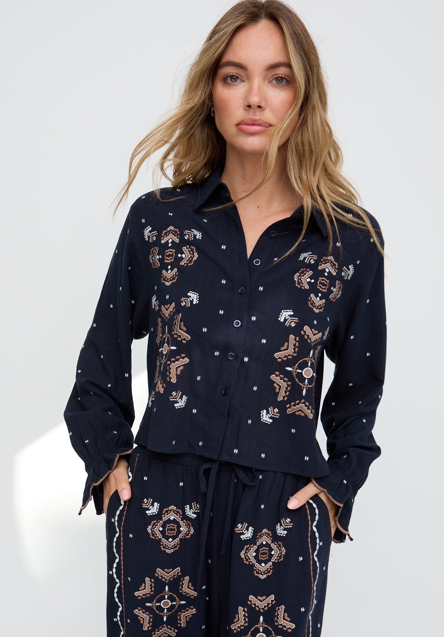 Woman wearing a dark blue embroidered shirt and pants on a white background