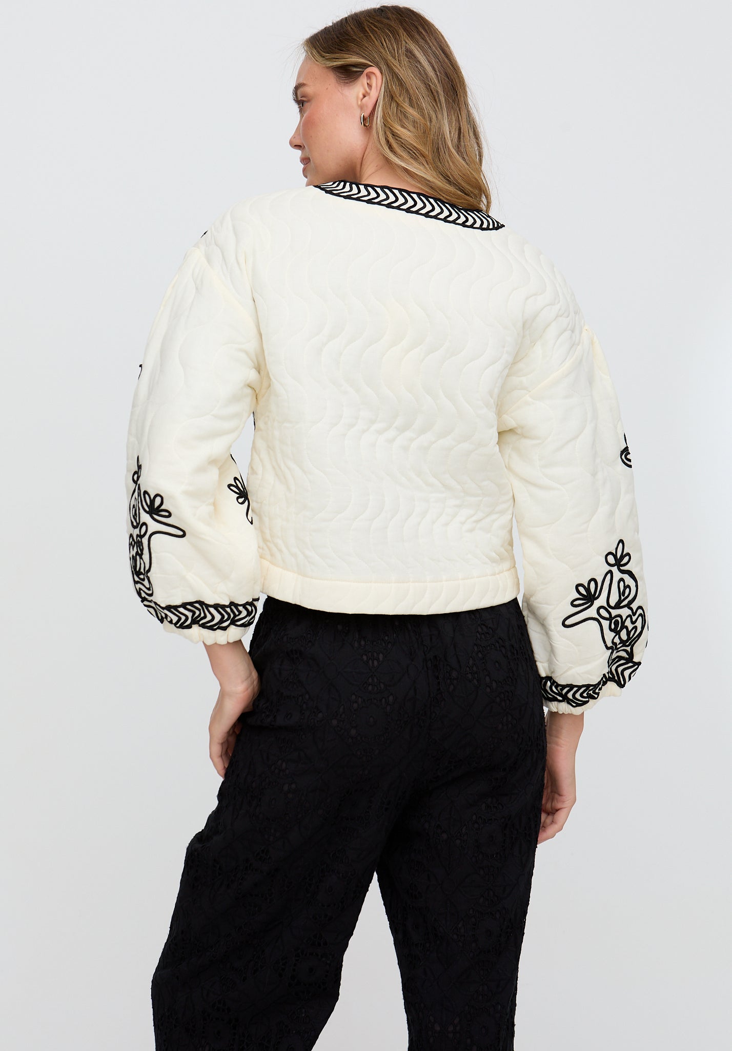 Person wearing a white quilted jacket with black embroidery on a plain background