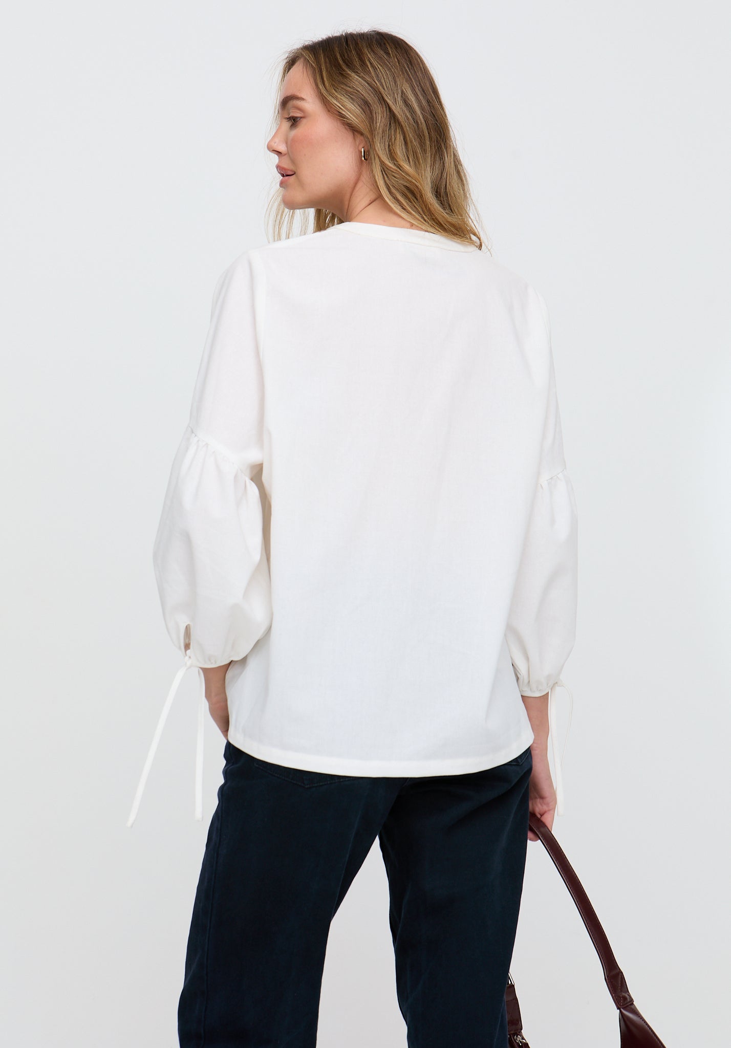 Woman wearing a white blouse and dark pants against a plain background