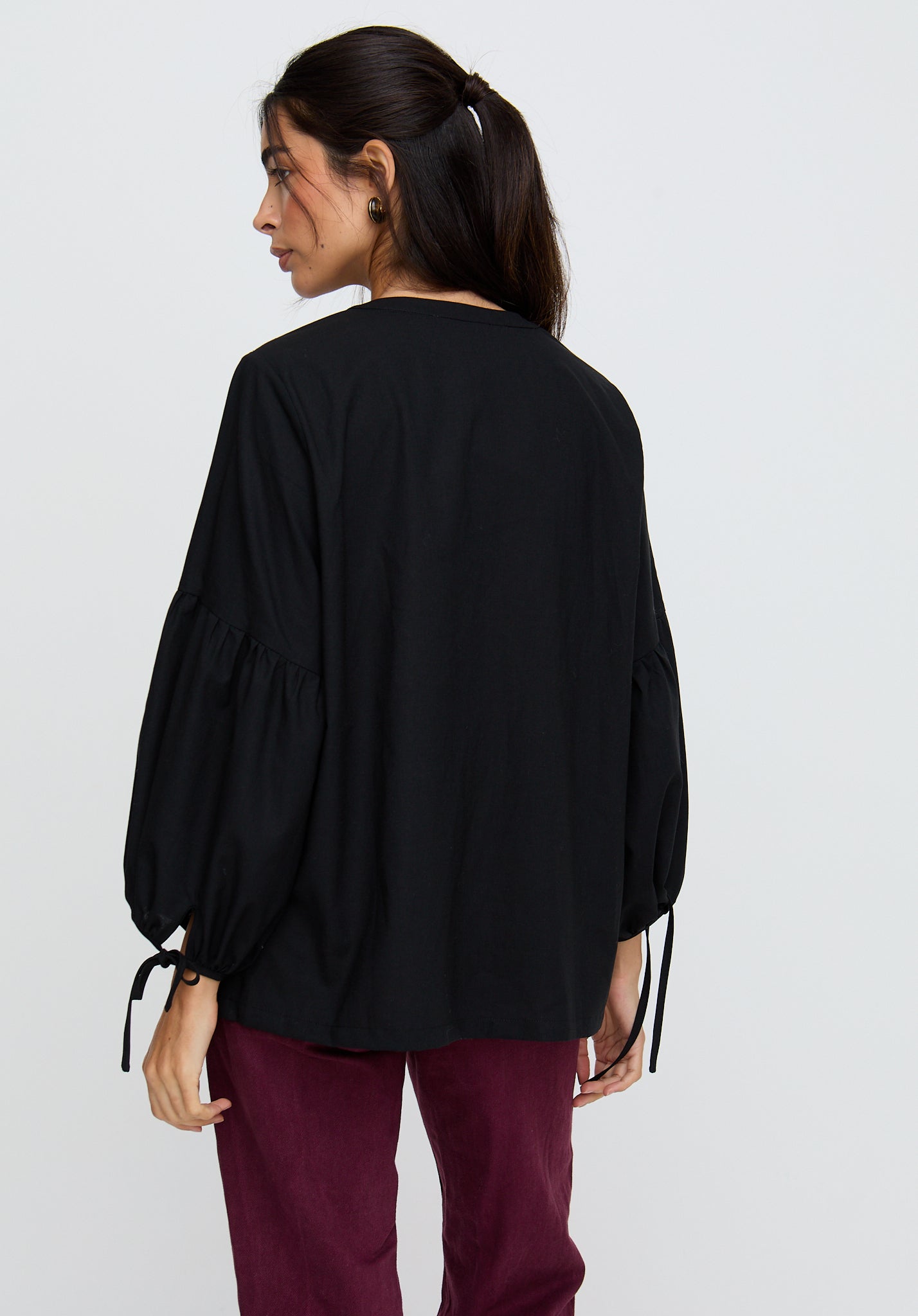 Person wearing a black blouse with balloon sleeves on a plain background