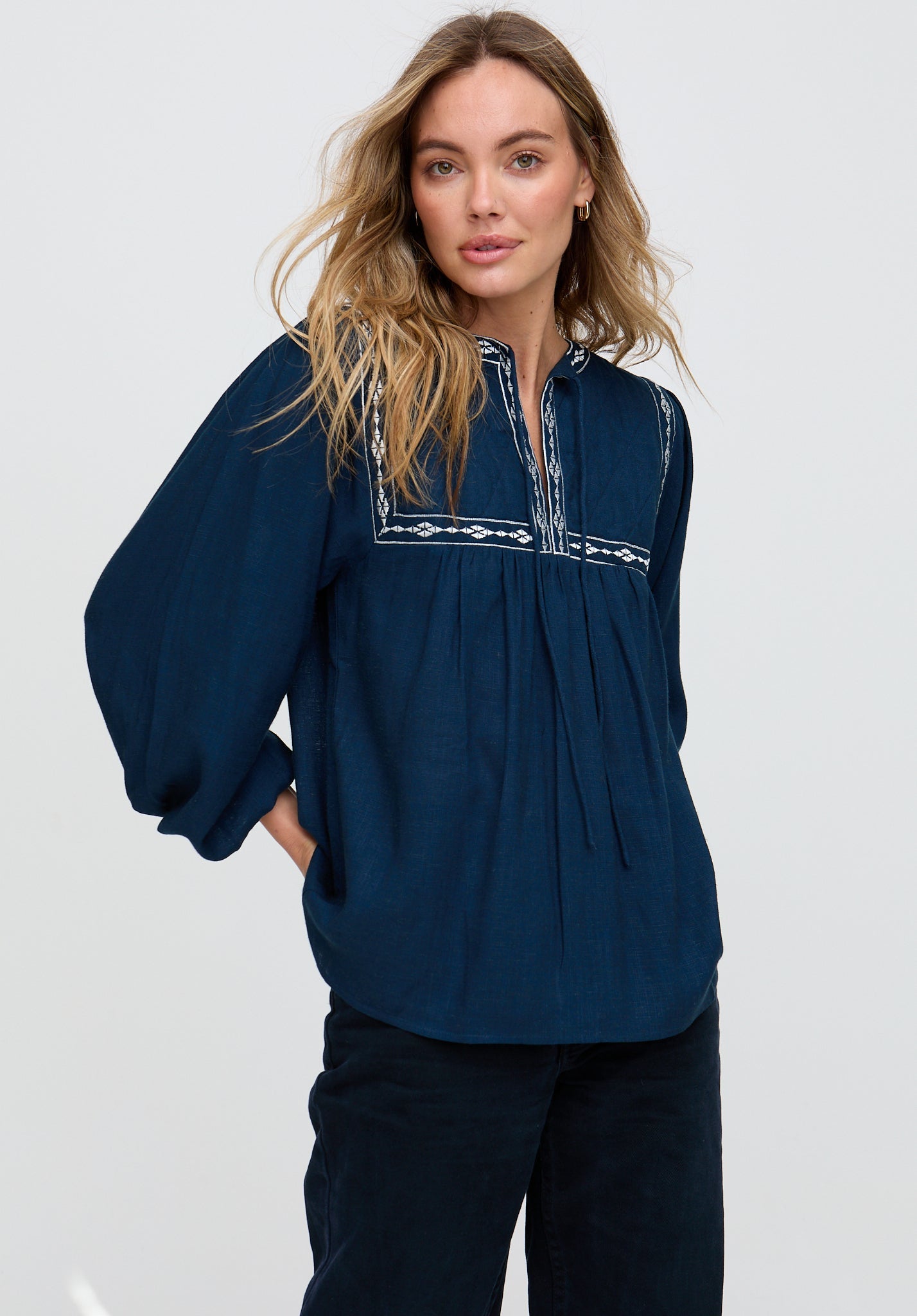 Woman wearing a navy blue blouse with embroidered details on a white background