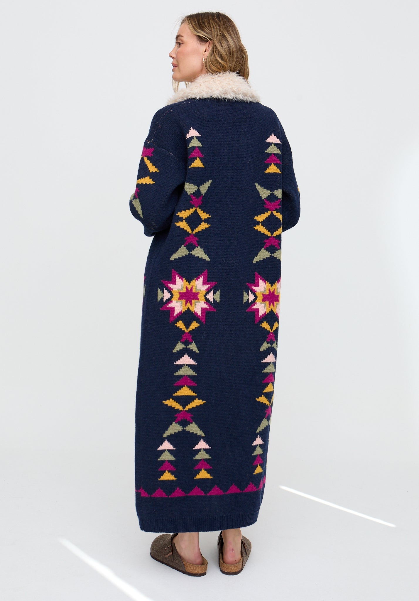 Woman wearing a long, dark blue patterned coat with a white background