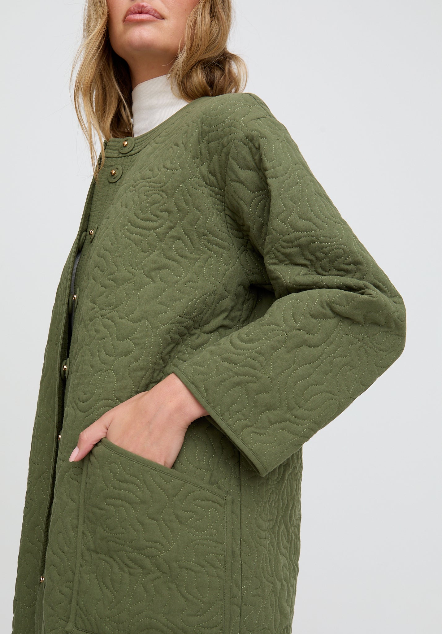 Green quilted coat worn by a person on a white background