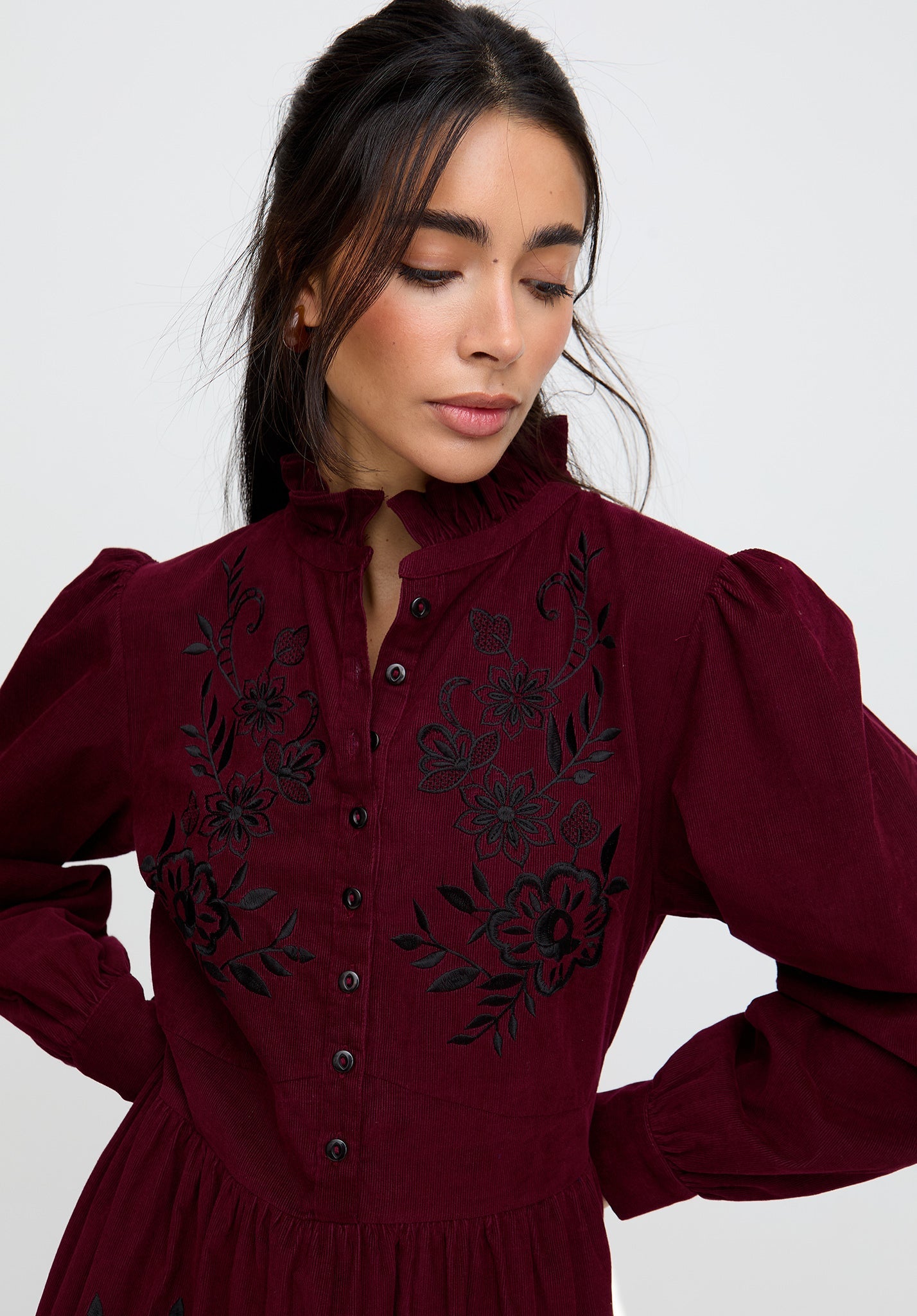 Woman wearing a burgundy dress with black floral embroidery on a plain background