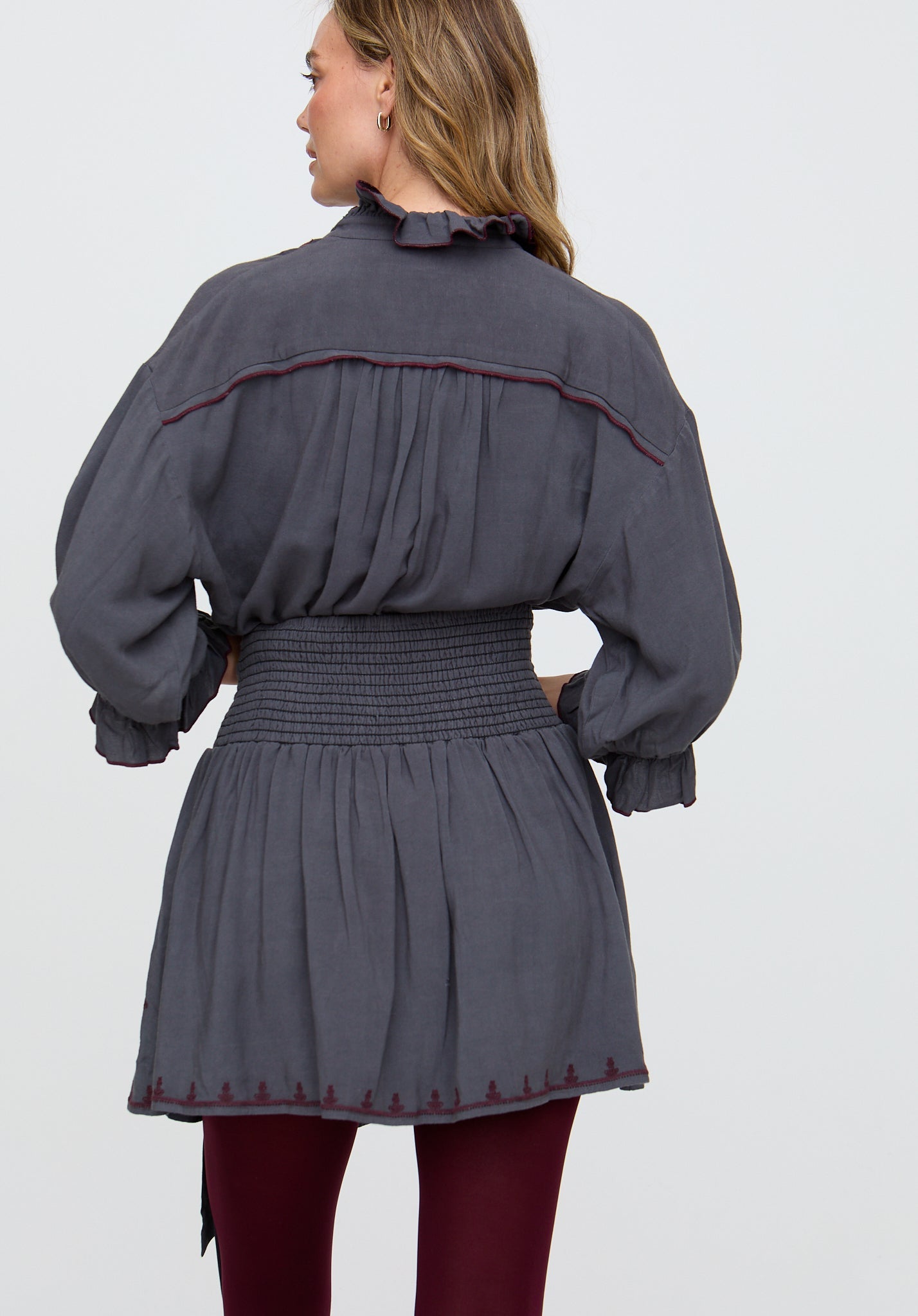 Woman wearing a gray dress with smocked waist and puffed sleeves on a light gray background