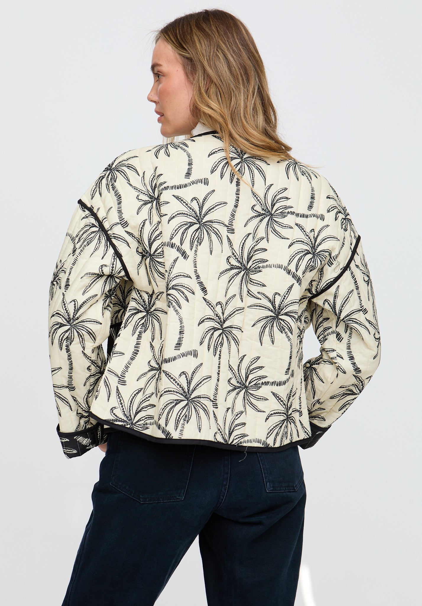 Woman wearing a cream jacket with black palm tree pattern on a white background