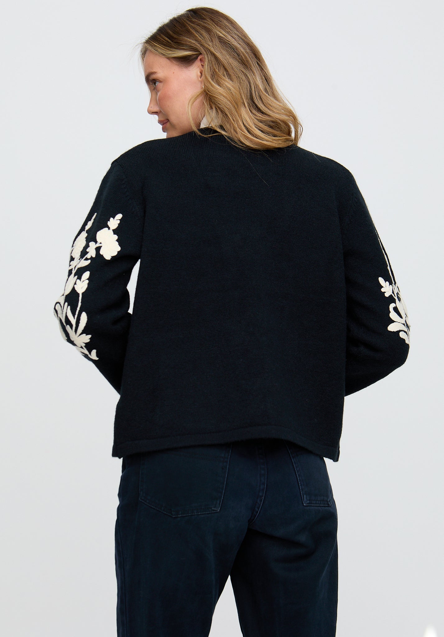 Person wearing a black jacket with white floral patterns on sleeves against a light gray background