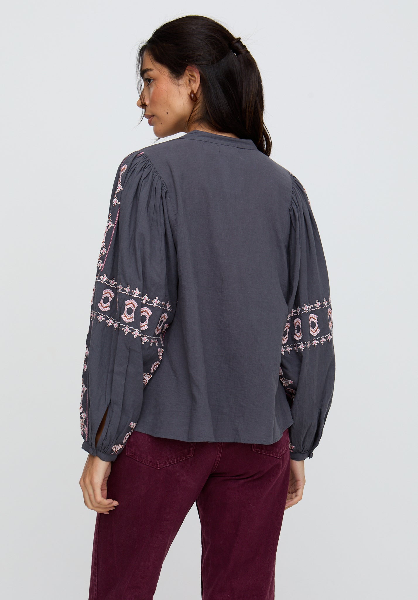 Woman wearing a dark gray long-sleeve top with intricate patterns on the sleeves against a white background