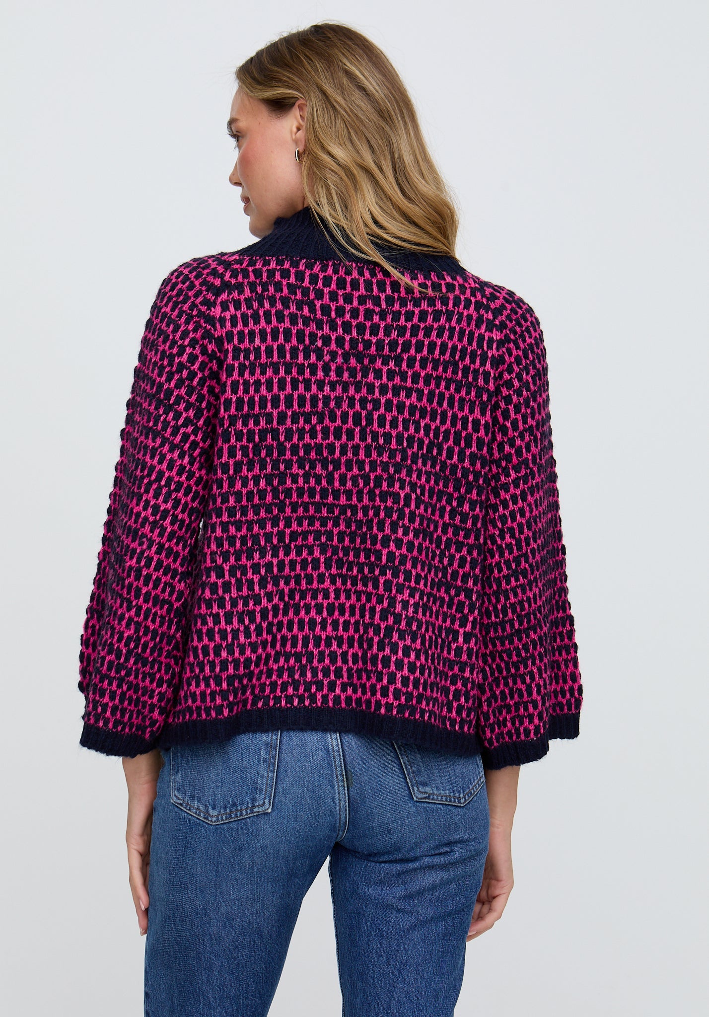 Person wearing a patterned jacket and jeans on a plain background