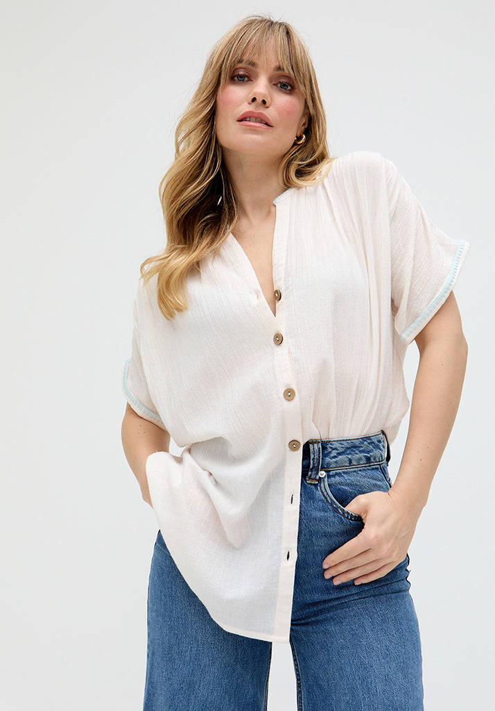 A woman wearing a cream-colored button-down shirt with cropped sleeves and jeans.