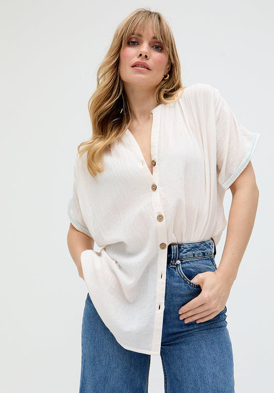 A woman wearing a cream-colored button-down shirt with cropped sleeves and jeans.