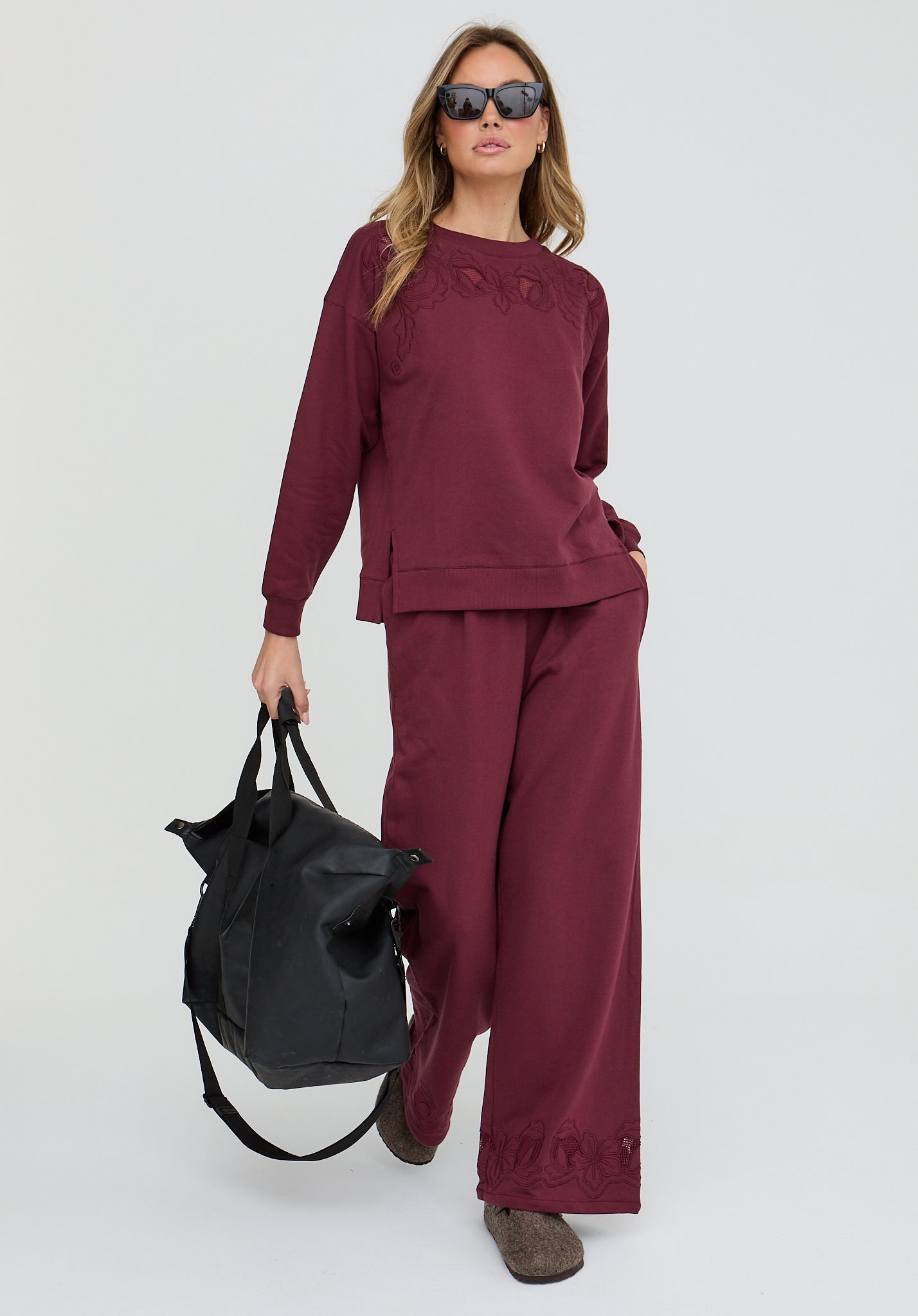 Woman in burgundy outfit holding a black bag on a white background