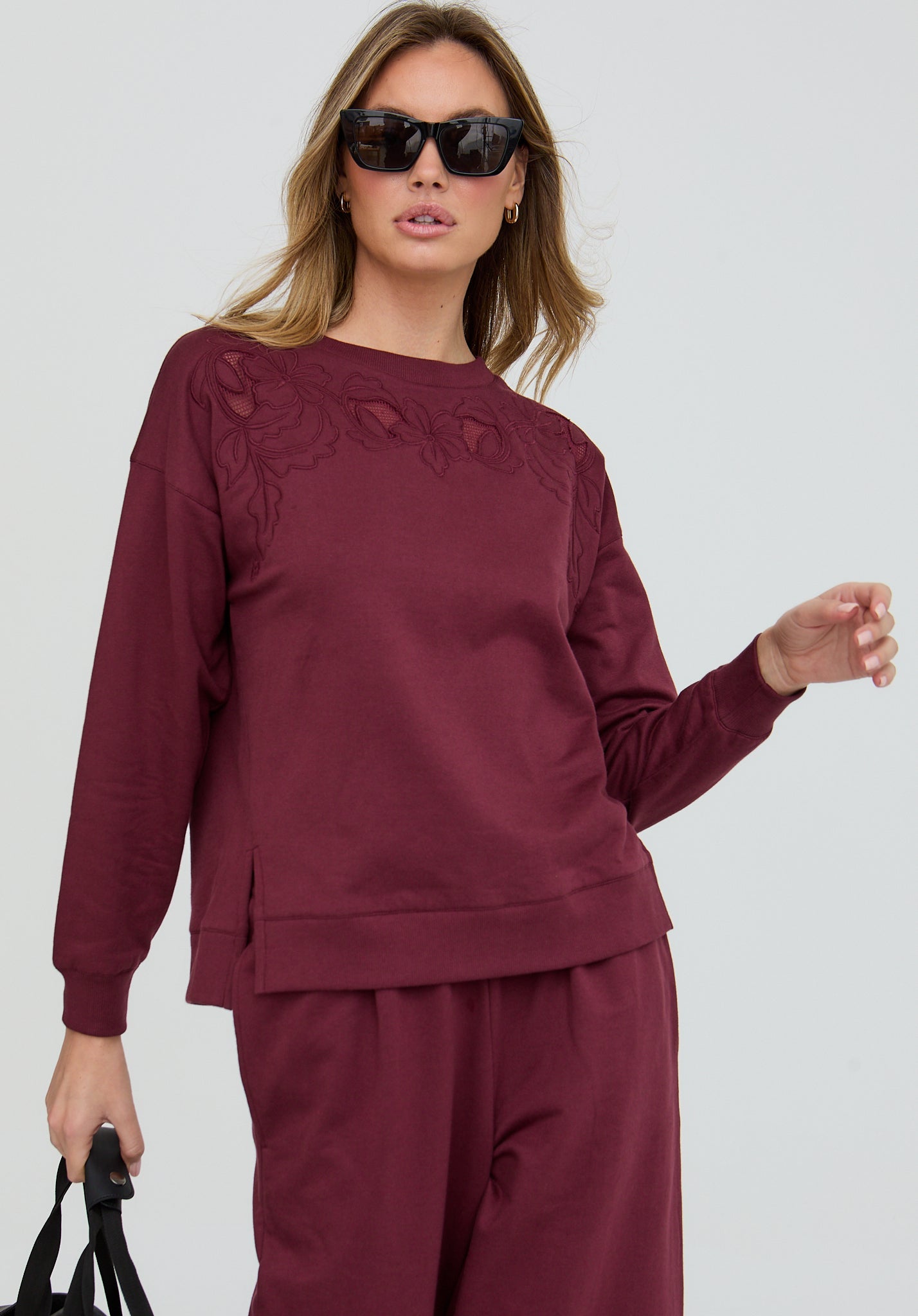 Woman wearing a burgundy sweatshirt and pants set on a light gray background