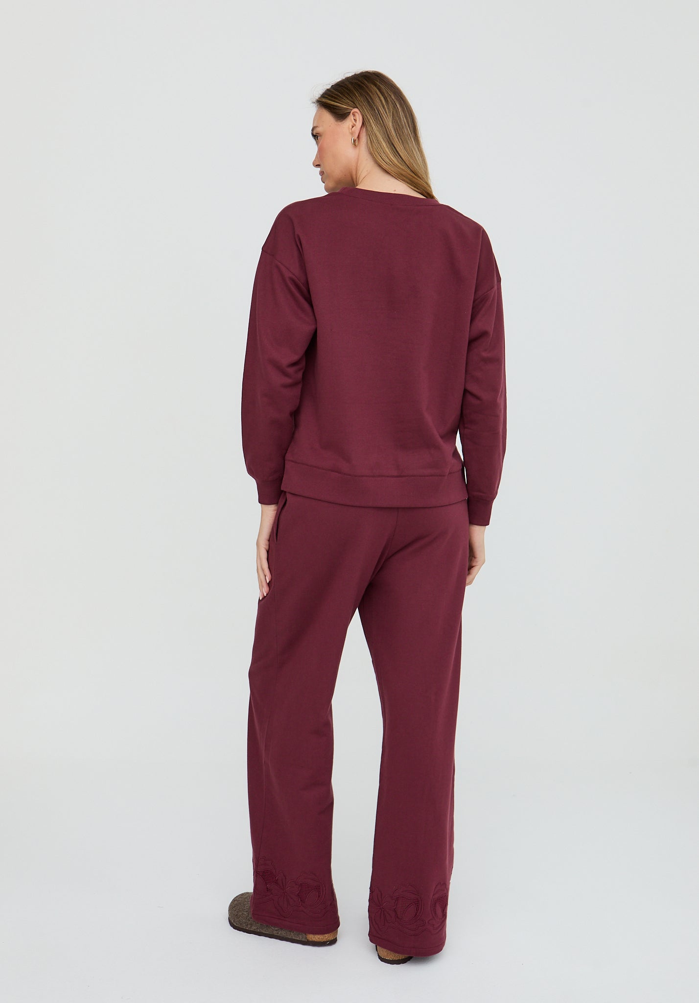 Woman wearing a burgundy sweatshirt and pants on a white background