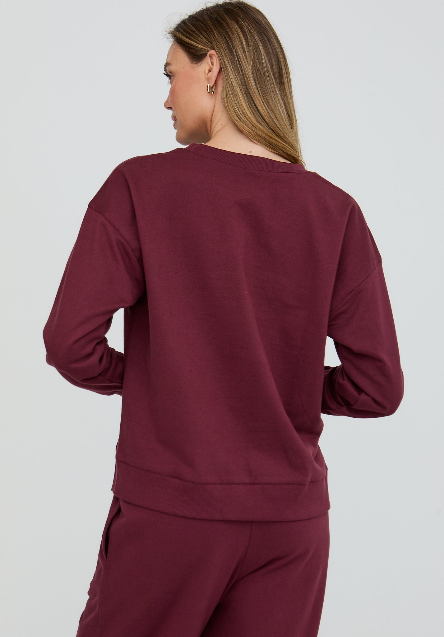 Person wearing a burgundy sweatshirt and pants on a white background