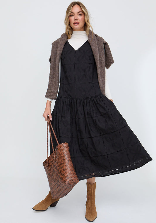 Woman wearing a black dress with a brown cardigan and holding a brown bag on a white background