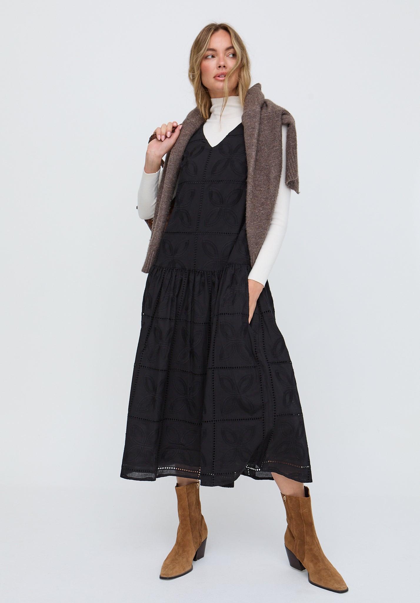 Woman wearing a black dress with a brown vest and tan boots on a white background