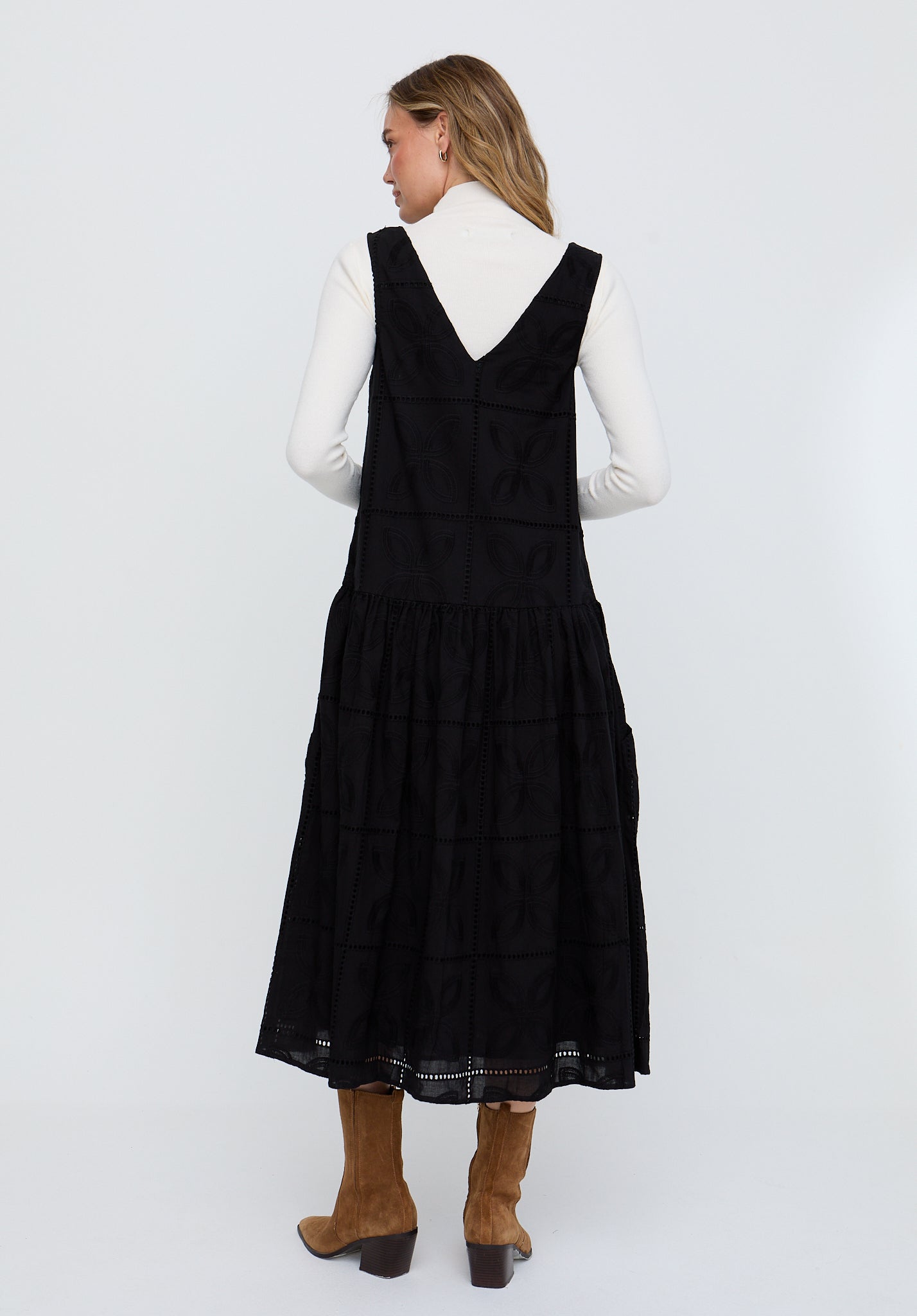 Woman wearing a black pinafore dress with a white shirt underneath on a white background