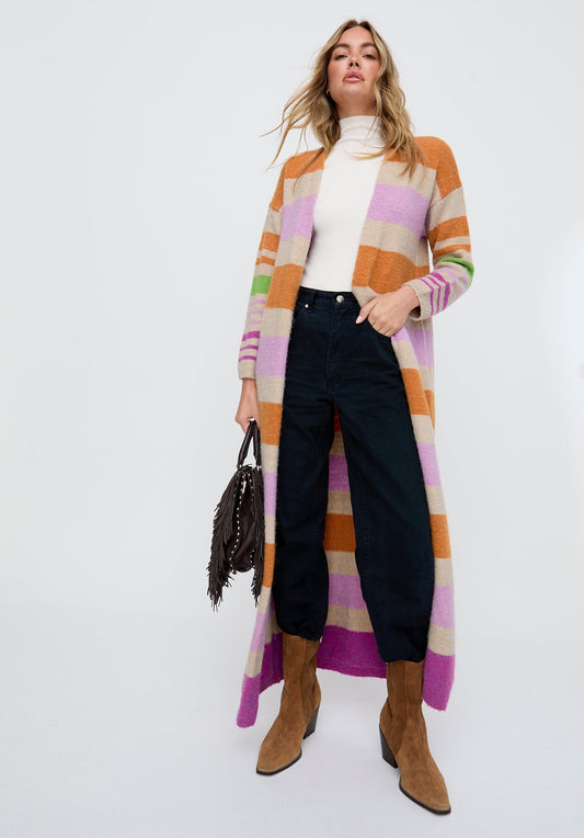 Woman wearing a long, colorful cardigan over a white top with black pants and brown boots on a white background.