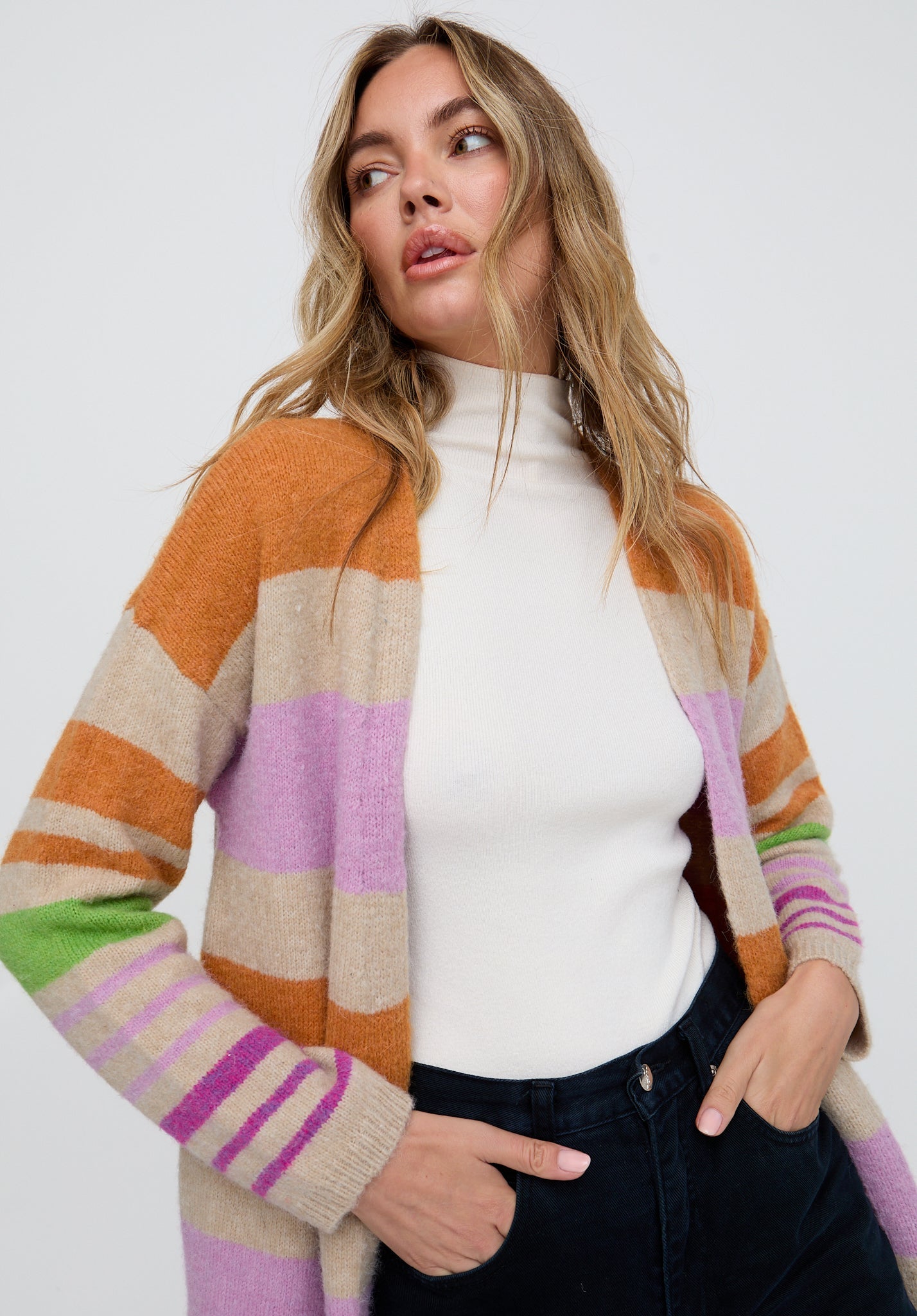 Woman wearing a colorful striped cardigan over a white turtleneck on a white background