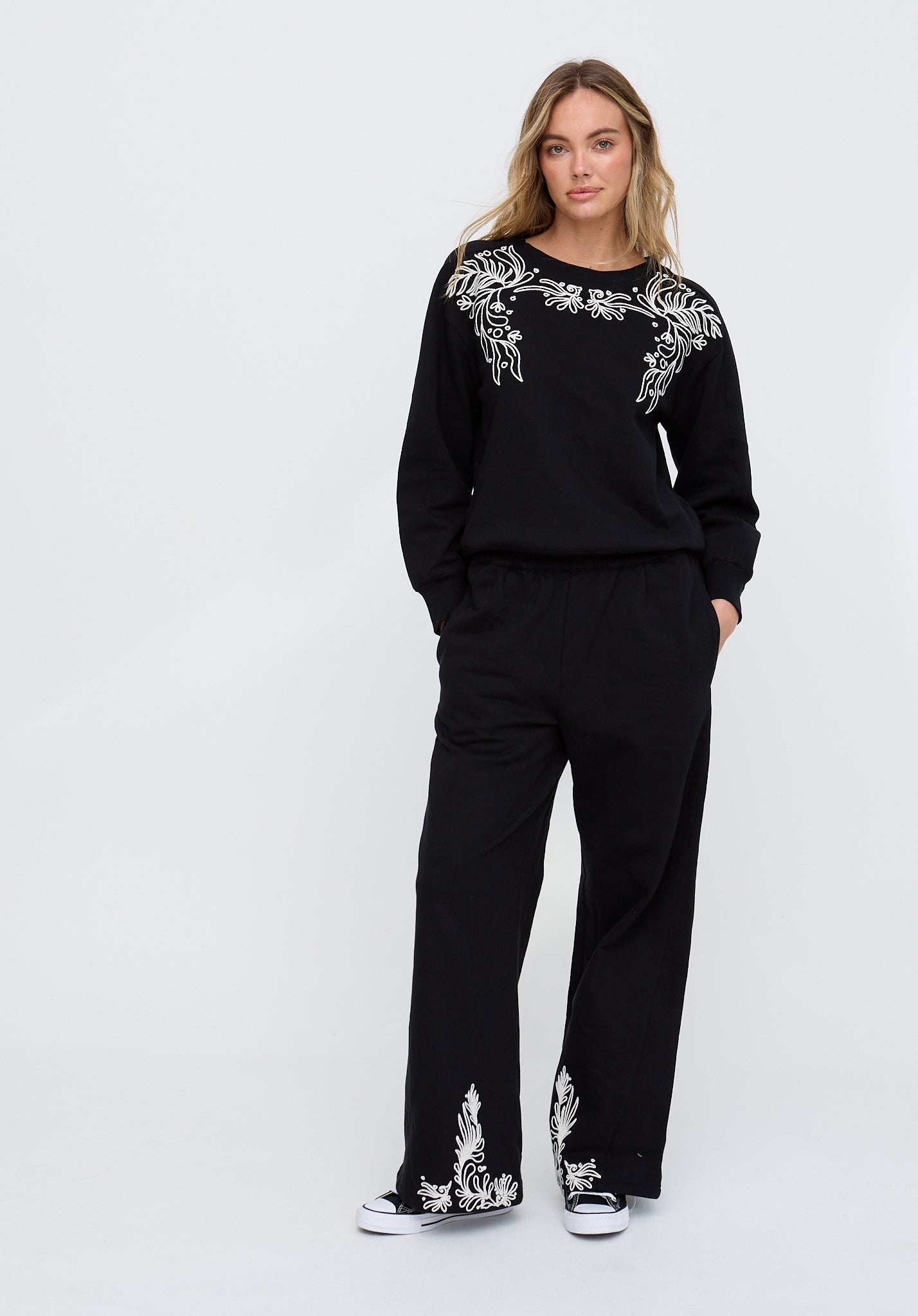 Woman wearing a black outfit with white embroidery on a white background