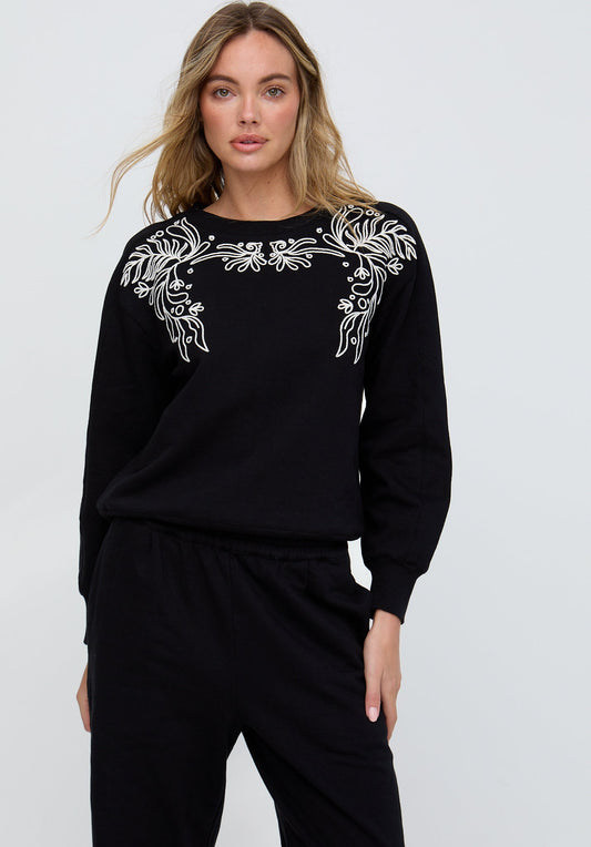 Woman wearing a black outfit with white floral embroidery on a plain background