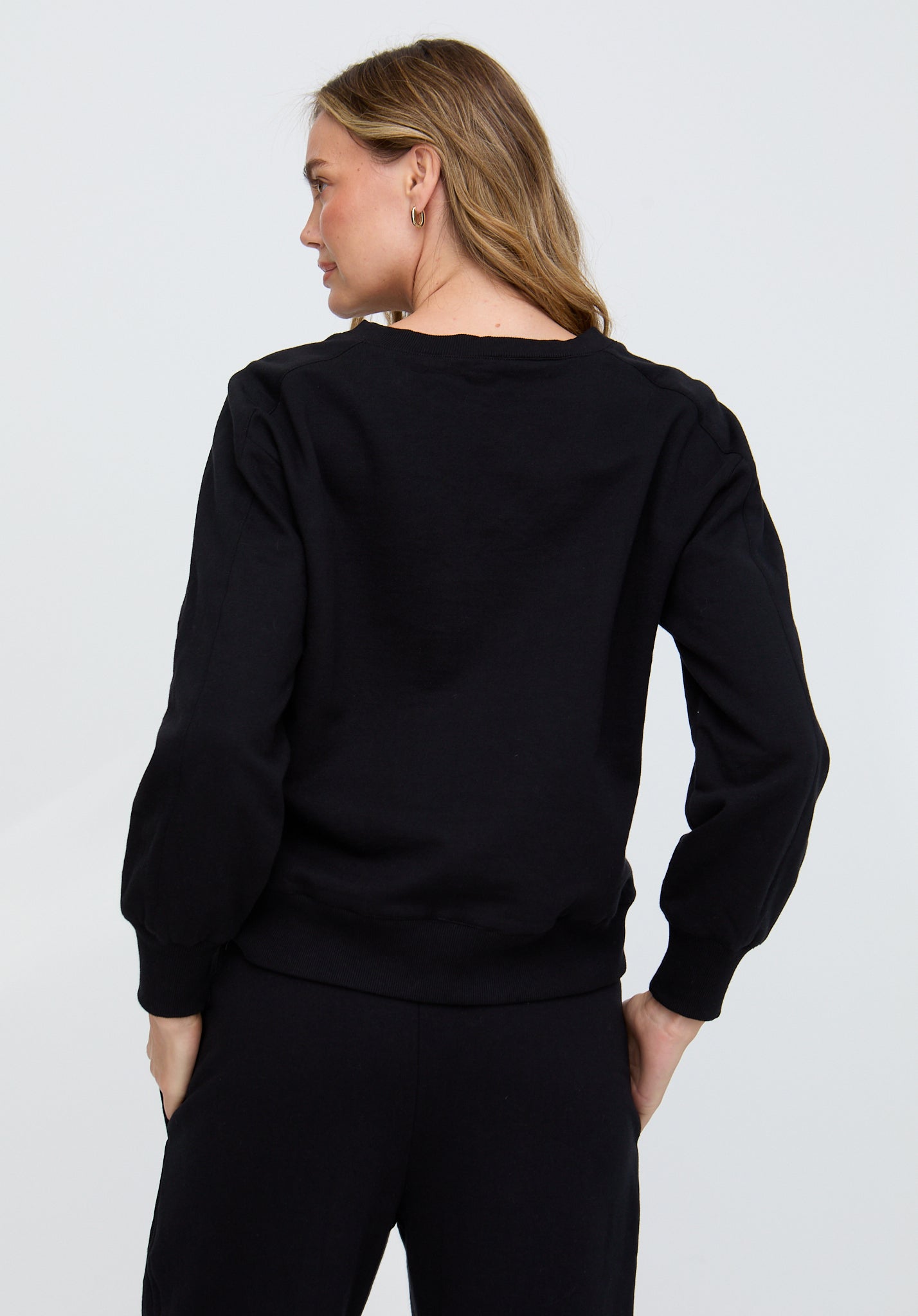 Person wearing a black sweater and pants on a plain background
