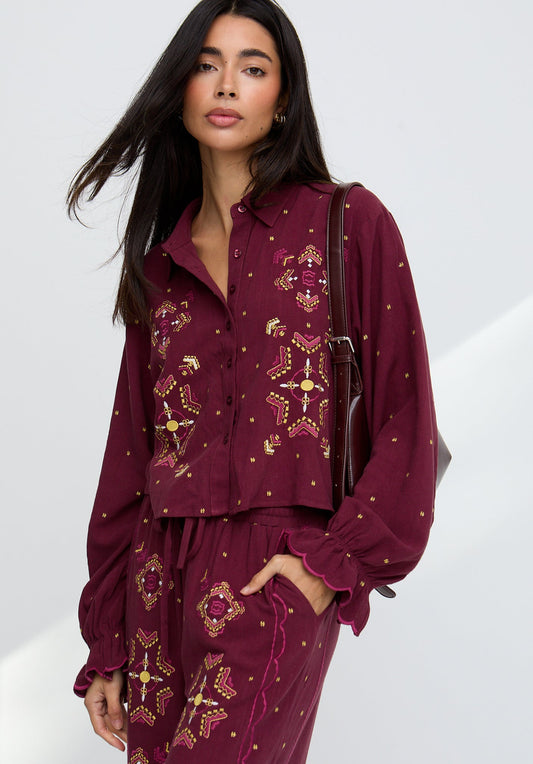 Woman wearing a burgundy outfit with gold patterns on a white background