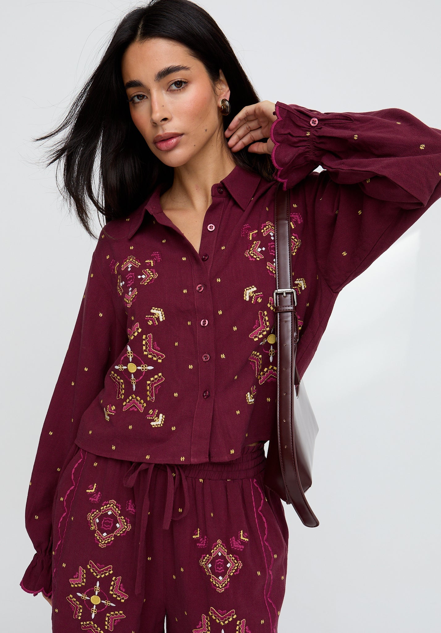 Woman wearing a burgundy embroidered outfit with a white background