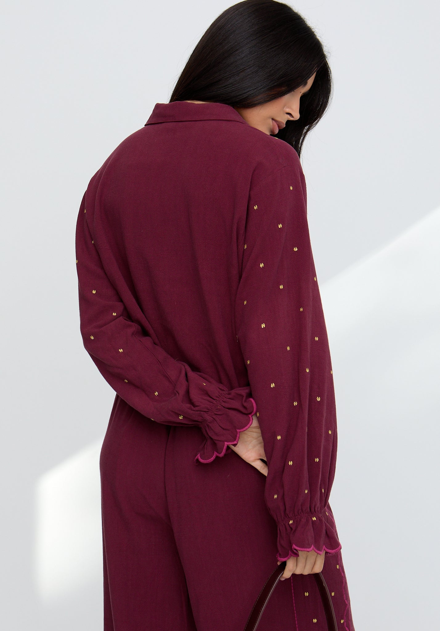 Woman wearing a burgundy outfit with gold embellishments on a white background