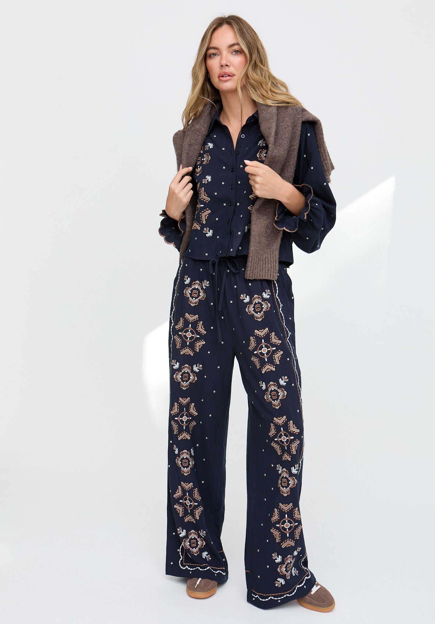 Woman wearing a navy patterned outfit with a brown vest on a white background
