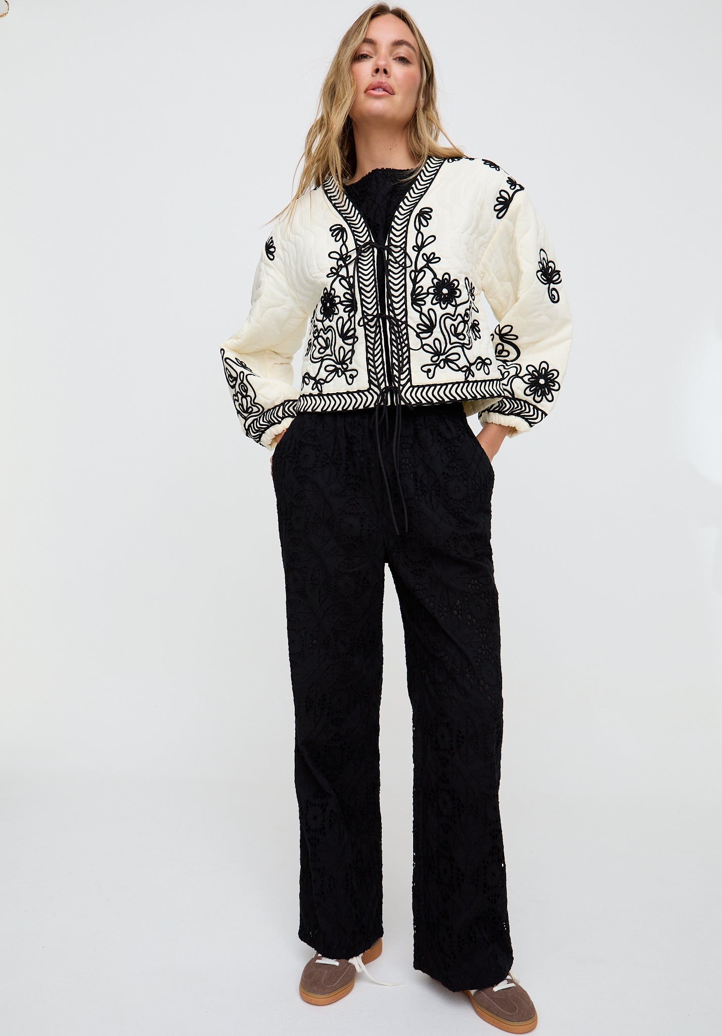 Woman wearing a white jacket with black floral patterns and black pants on a white background
