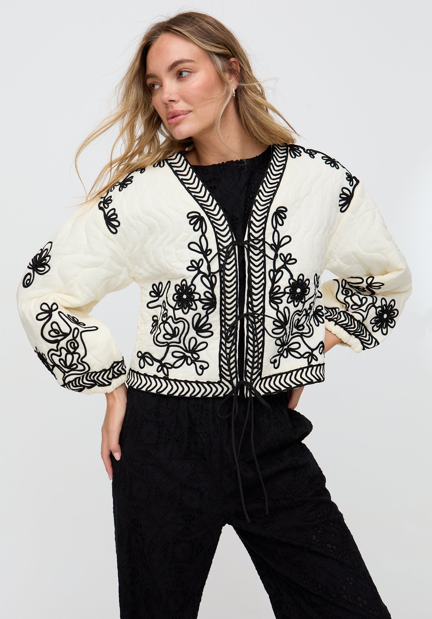 Woman wearing a white embroidered jacket with black patterns on a plain background