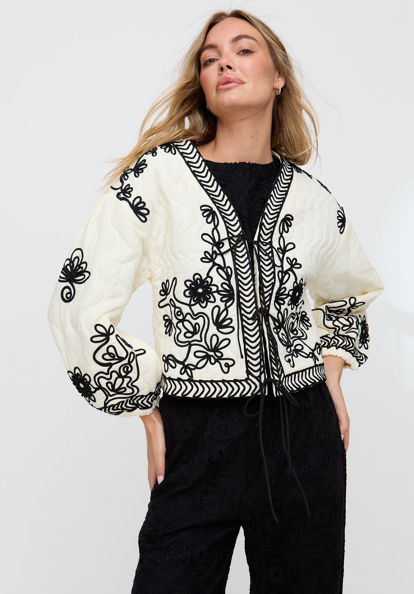 Woman wearing a white blouse with black embroidery on a plain background