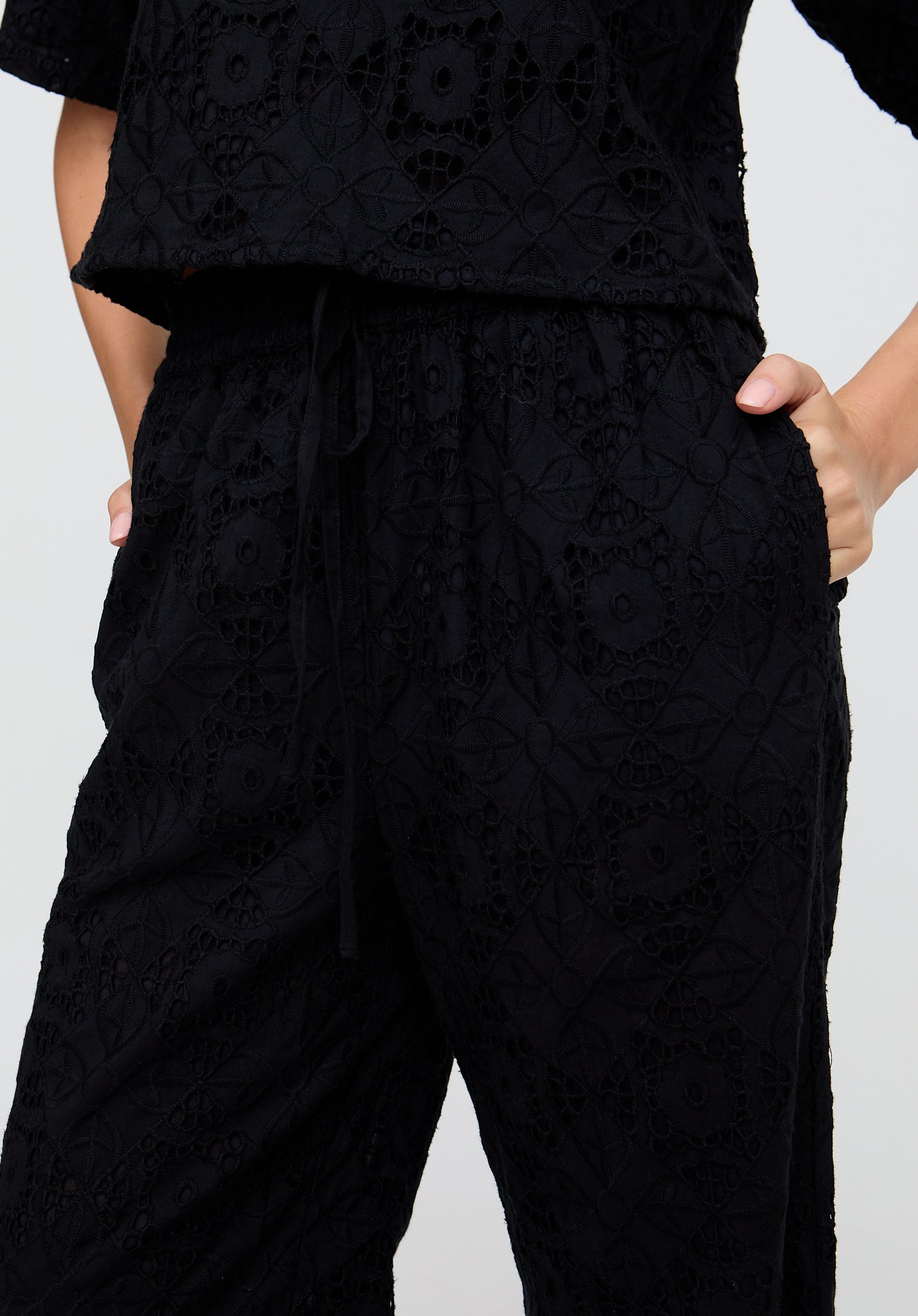 Person wearing a black textured outfit with wide-leg pants and a cropped top on a light gray background