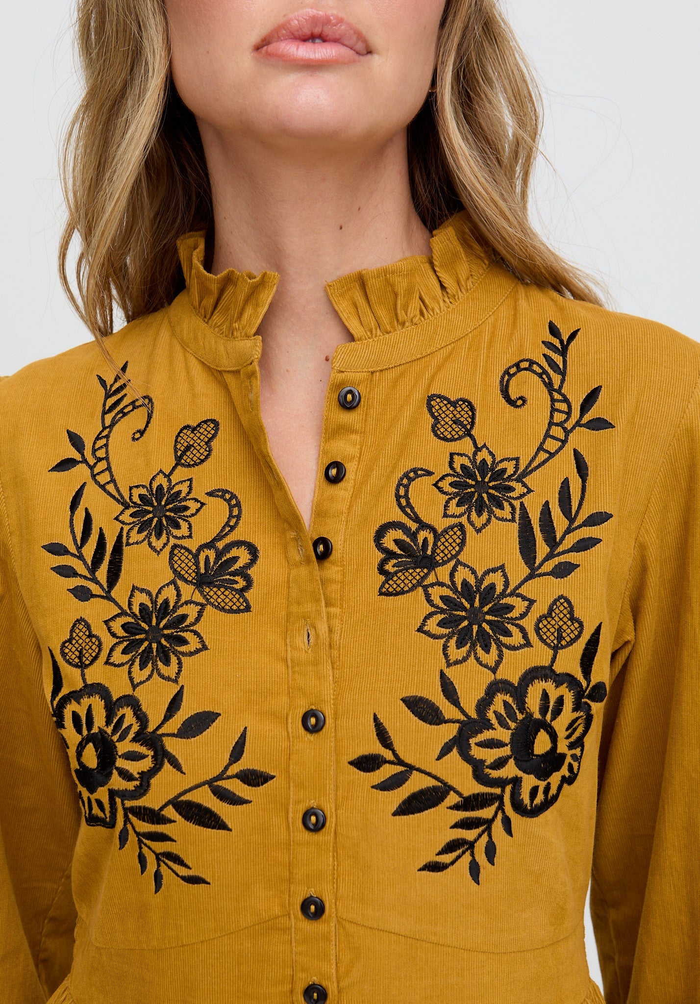 Mustard yellow blouse with black floral embroidery on a white background