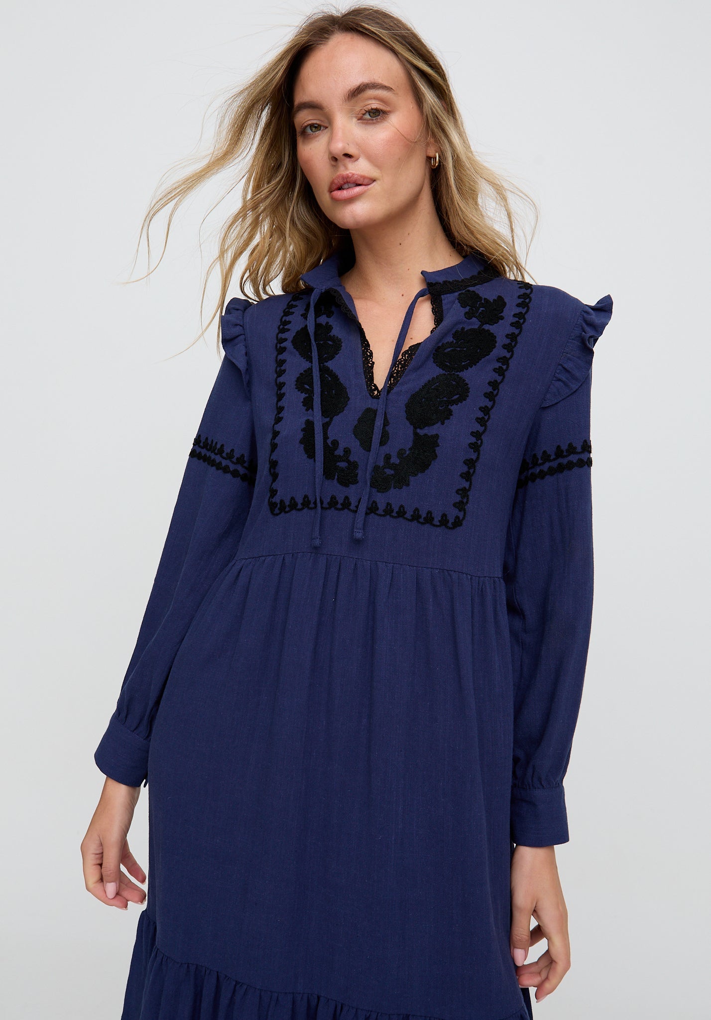 Woman wearing a navy blue dress with intricate black embroidery on a white background