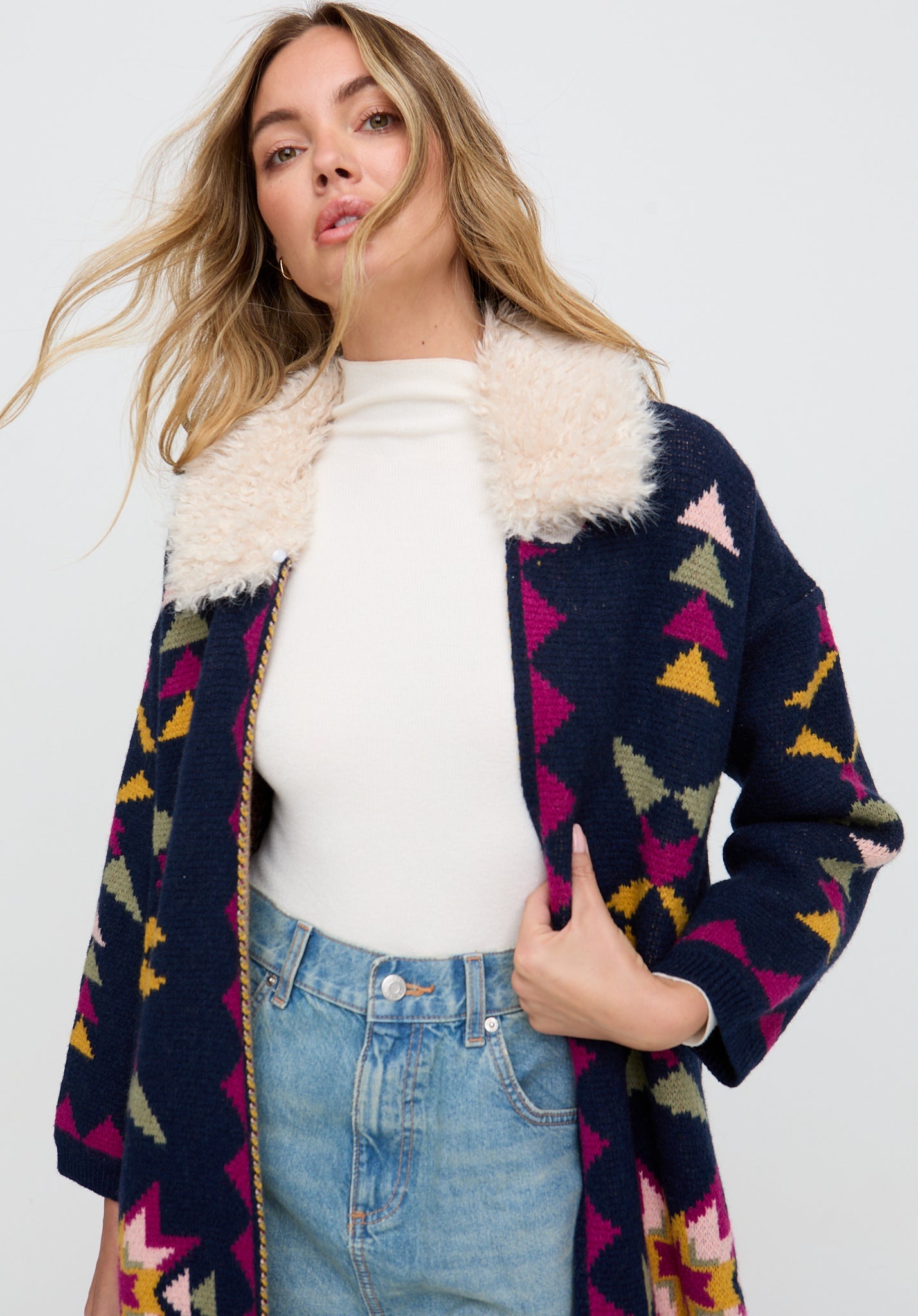 Woman wearing a colorful patterned cardigan with a white interior on a plain background