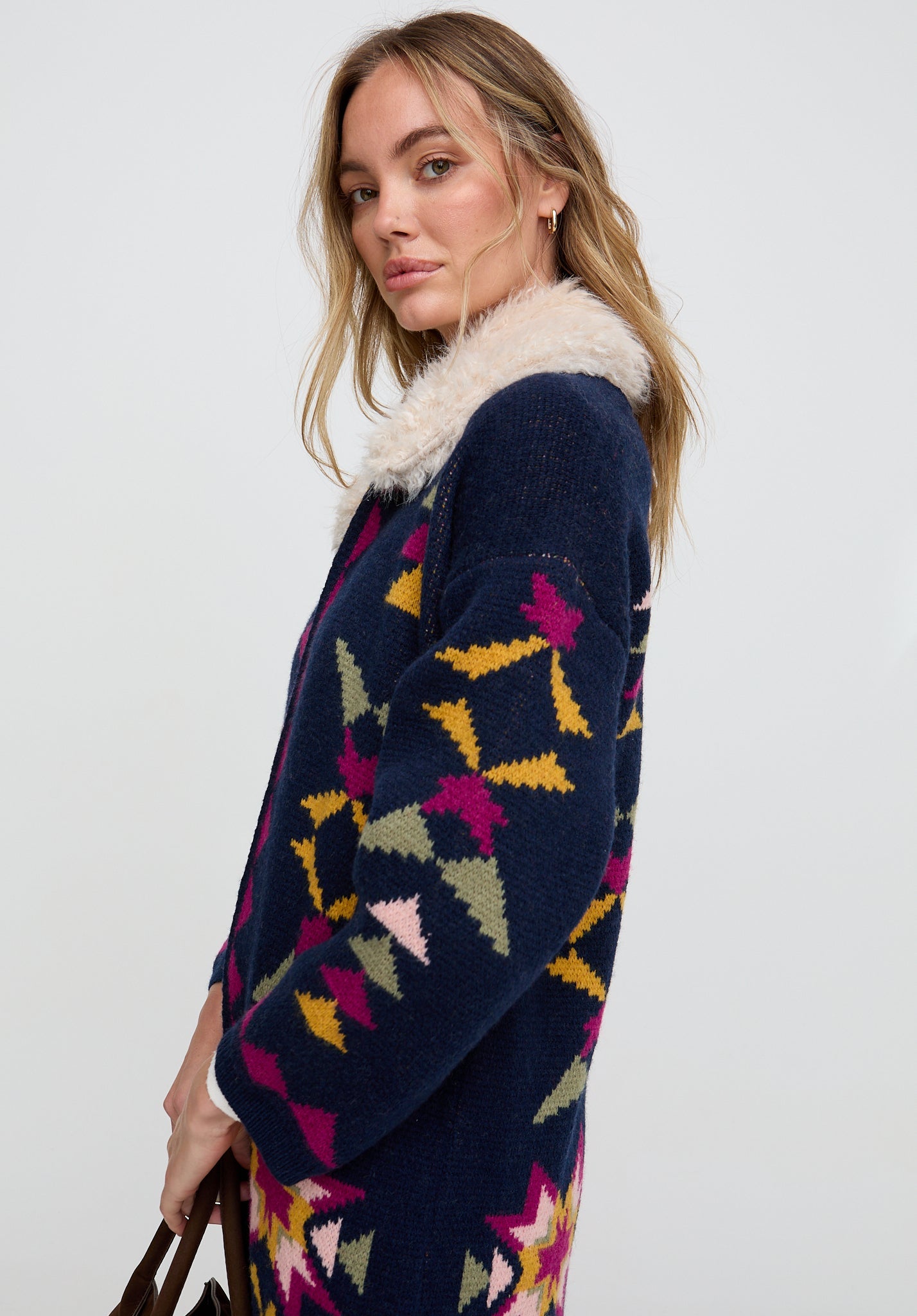 Woman wearing a navy cardigan with colorful geometric pattern and fur collar on a white background