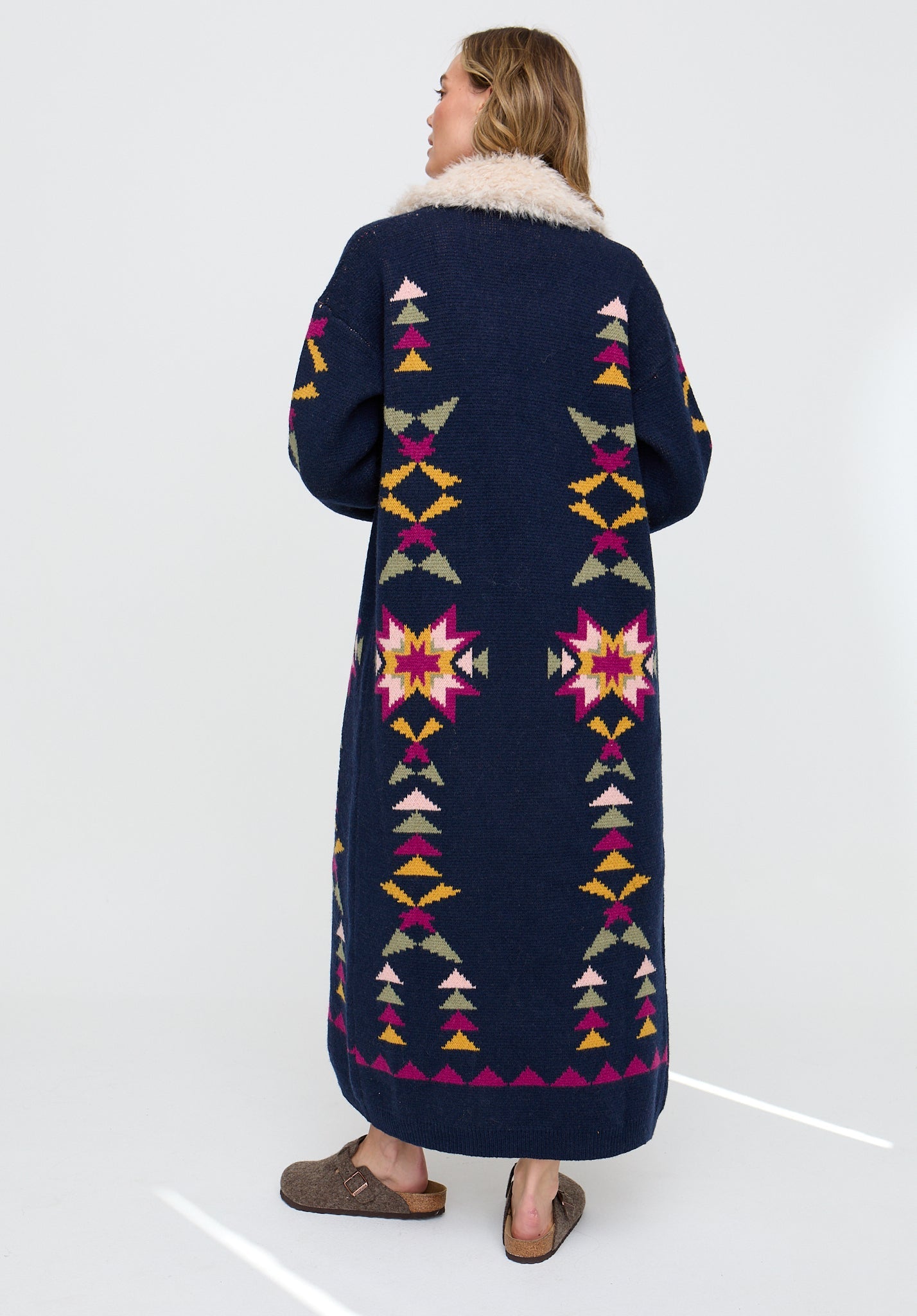 Person wearing a long, patterned coat with a white background