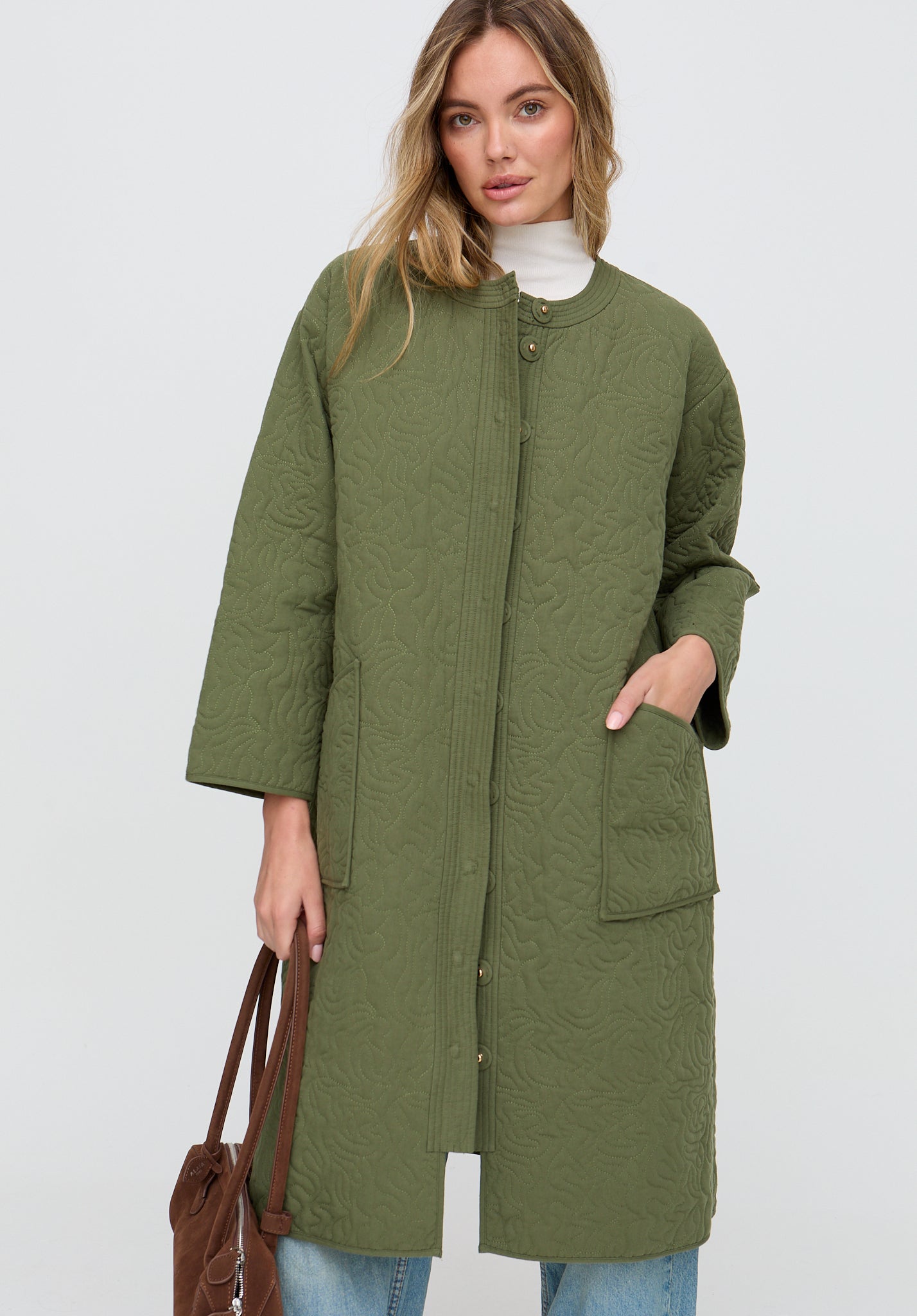 Woman wearing a green coat holding a brown bag on a white background