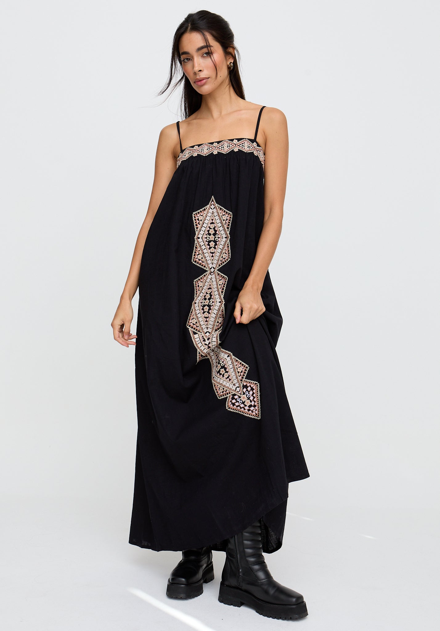 Woman wearing a black dress with intricate white embroidery on a white background