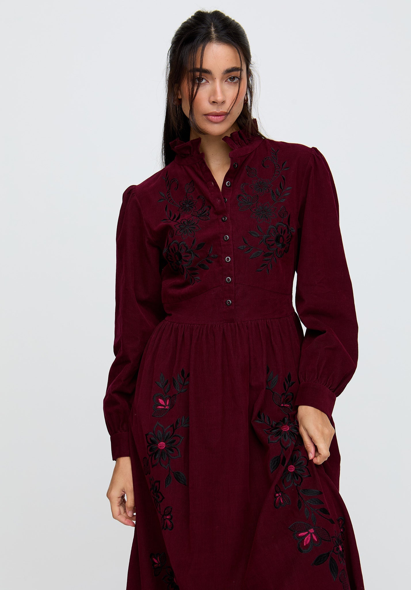 Woman wearing a burgundy dress with floral embroidery on a white background