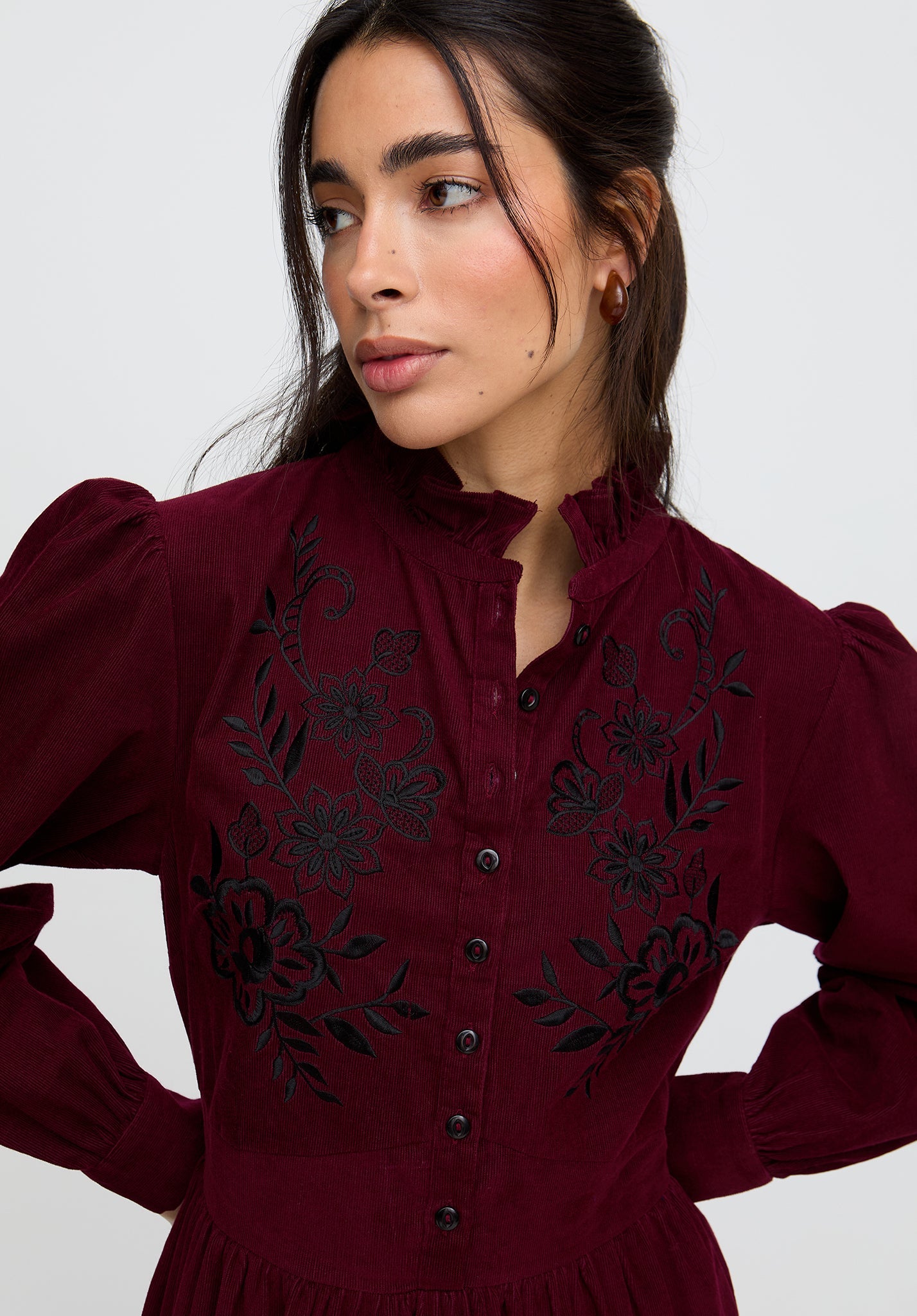 Woman wearing a burgundy dress with black floral embroidery against a white background