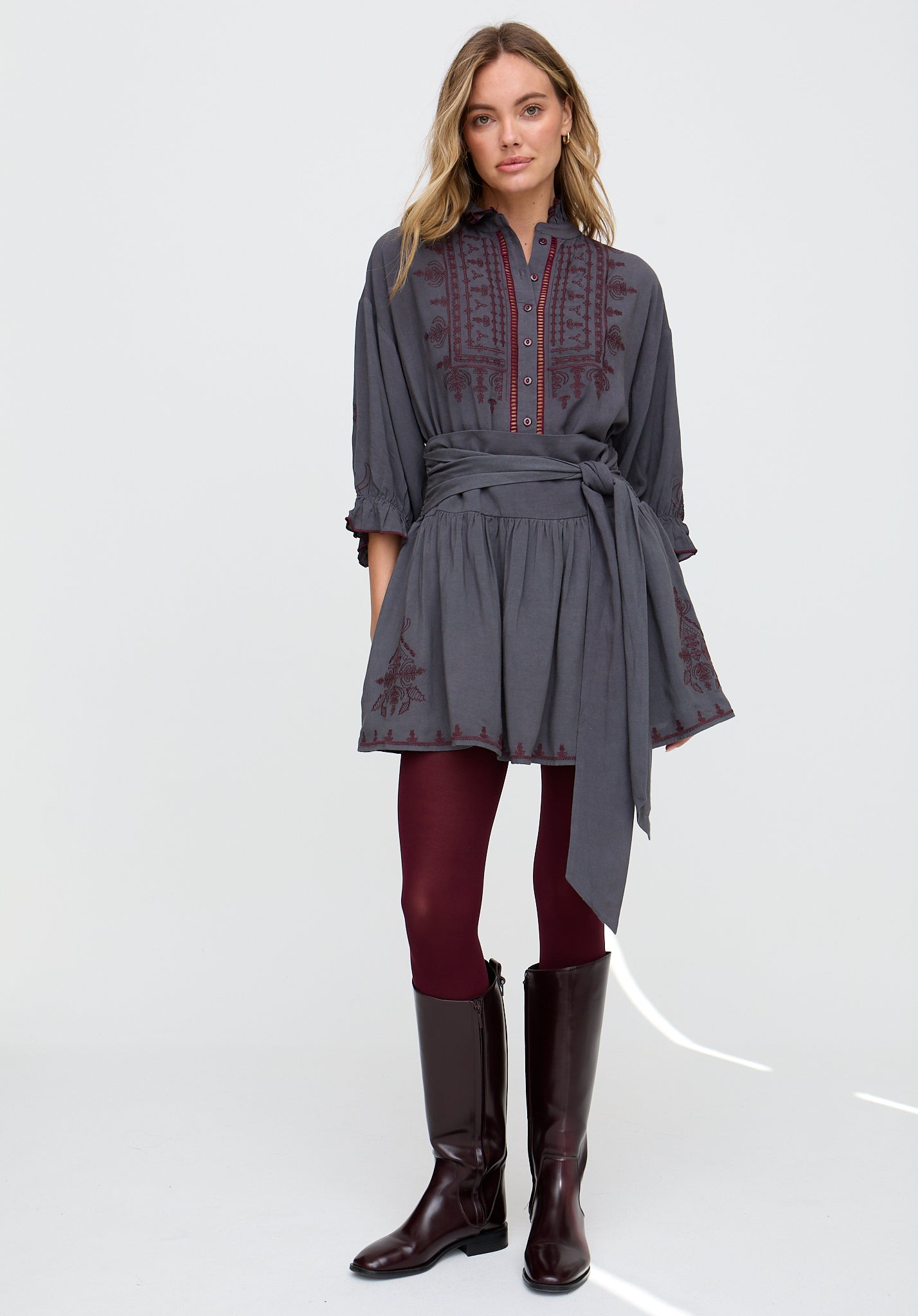 Woman wearing a gray dress with red embroidery and brown boots on a white background