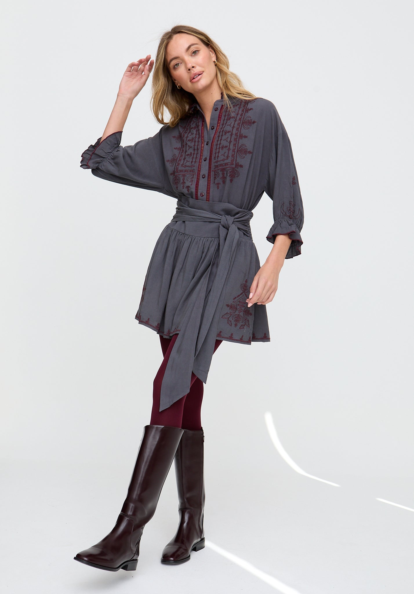 Woman wearing a dark gray dress with red embroidery and black boots on a white background